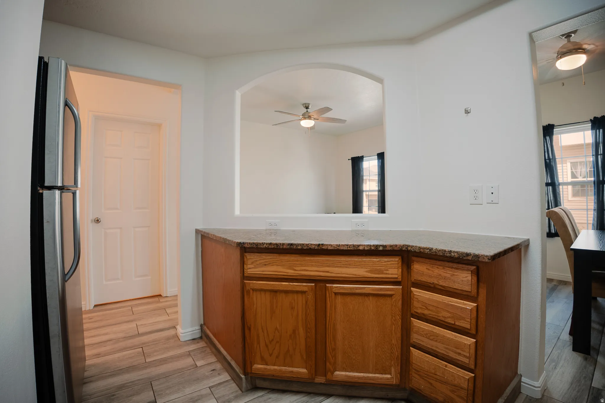 Kitchen featuring ceiling fan, freestanding refrigerator, light wood-style flooring, wood finish cabinetry, and light stone countertops