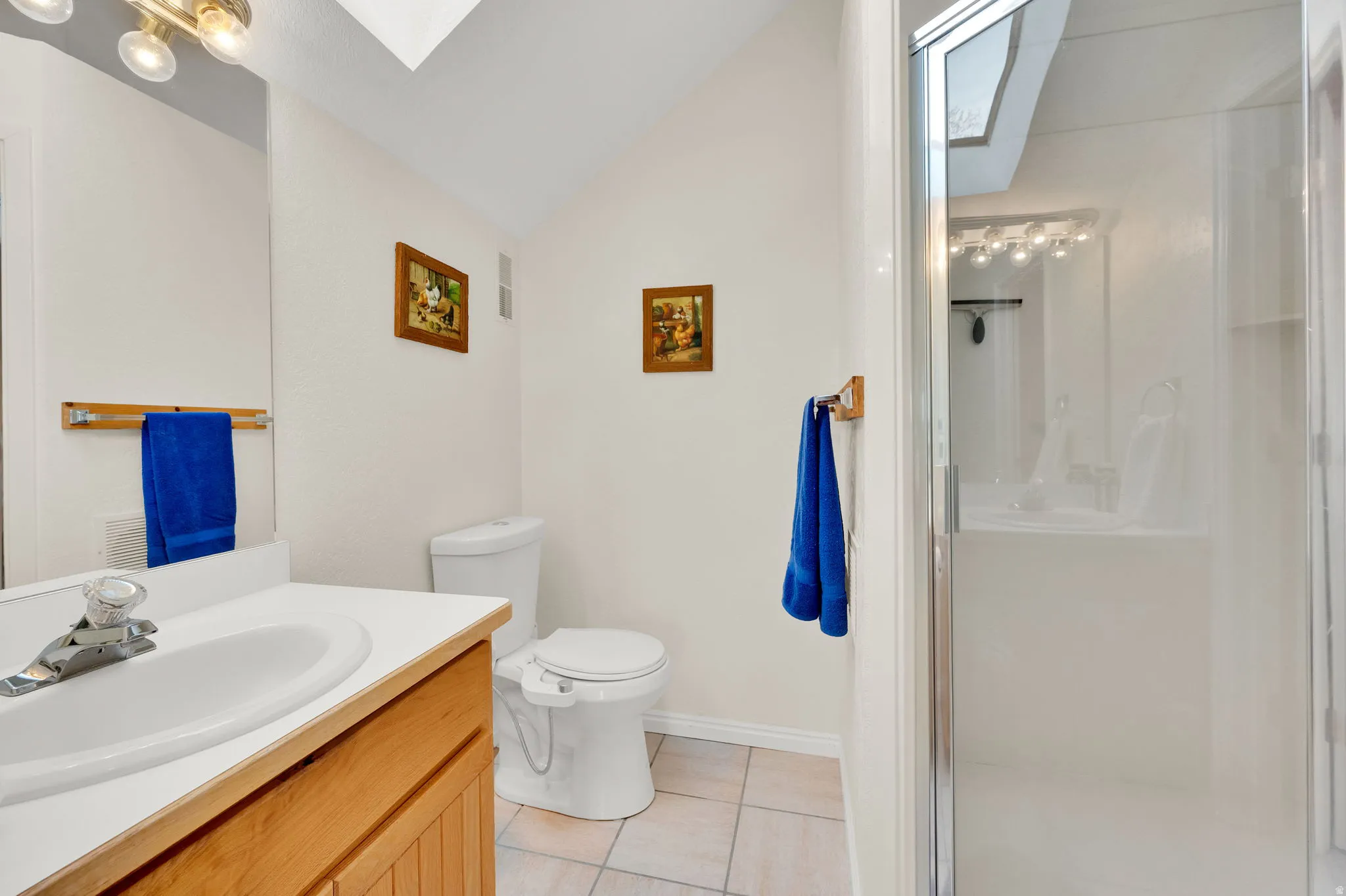 Bathroom featuring a skylight, vanity, a shower stall, light tile patterned floors, and lofted ceiling