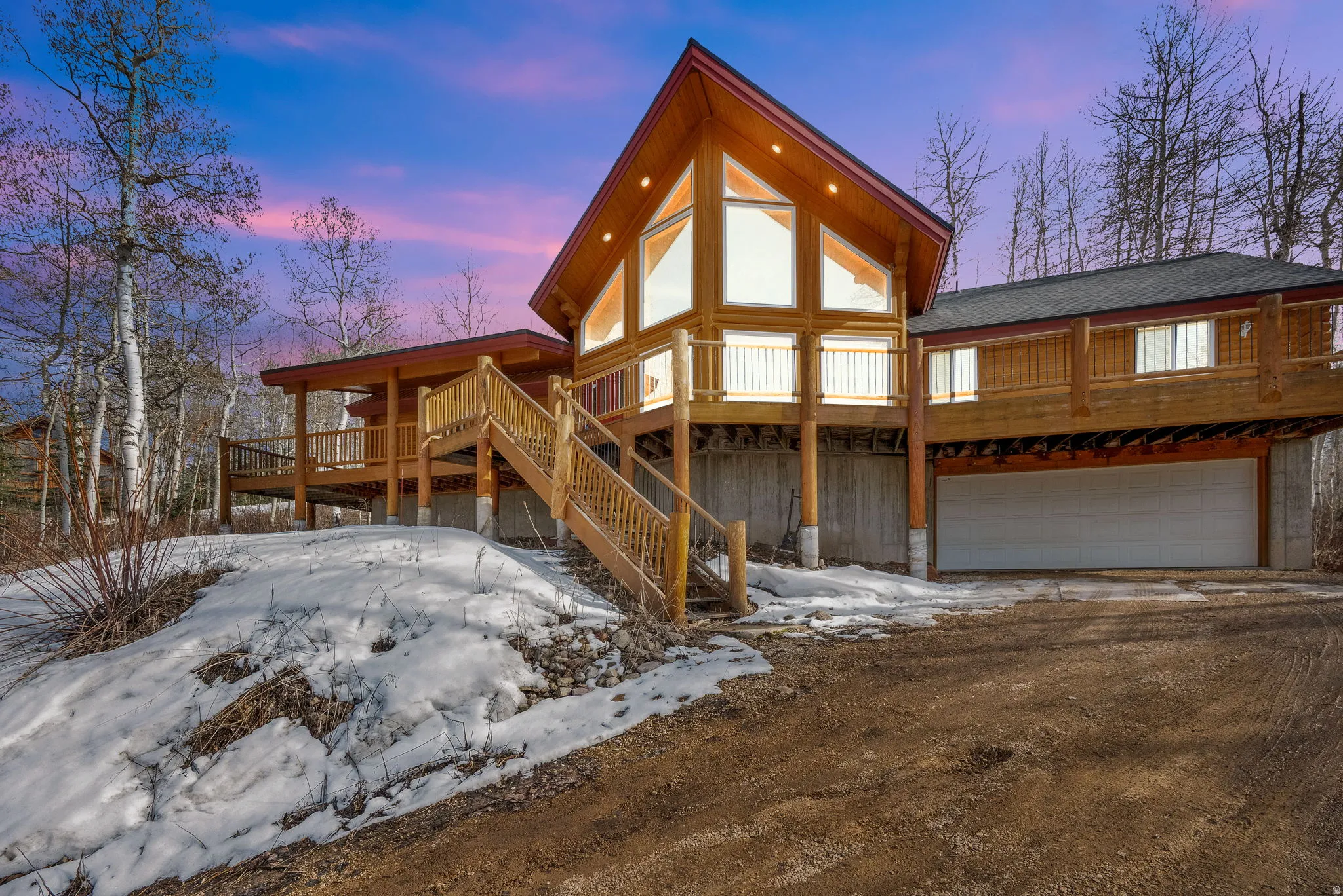 Snow covered rear of property with a deck, an attached garage, and dirt driveway