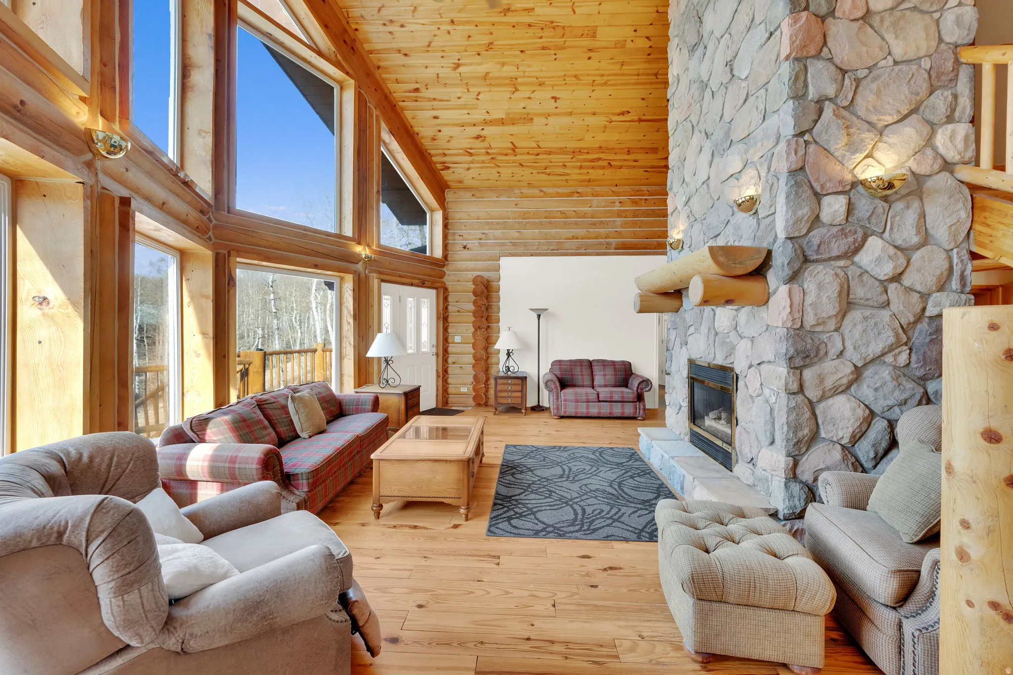 Living area with rustic walls, hardwood / wood-style floors, a stone fireplace, and a vaulted wooden ceiling