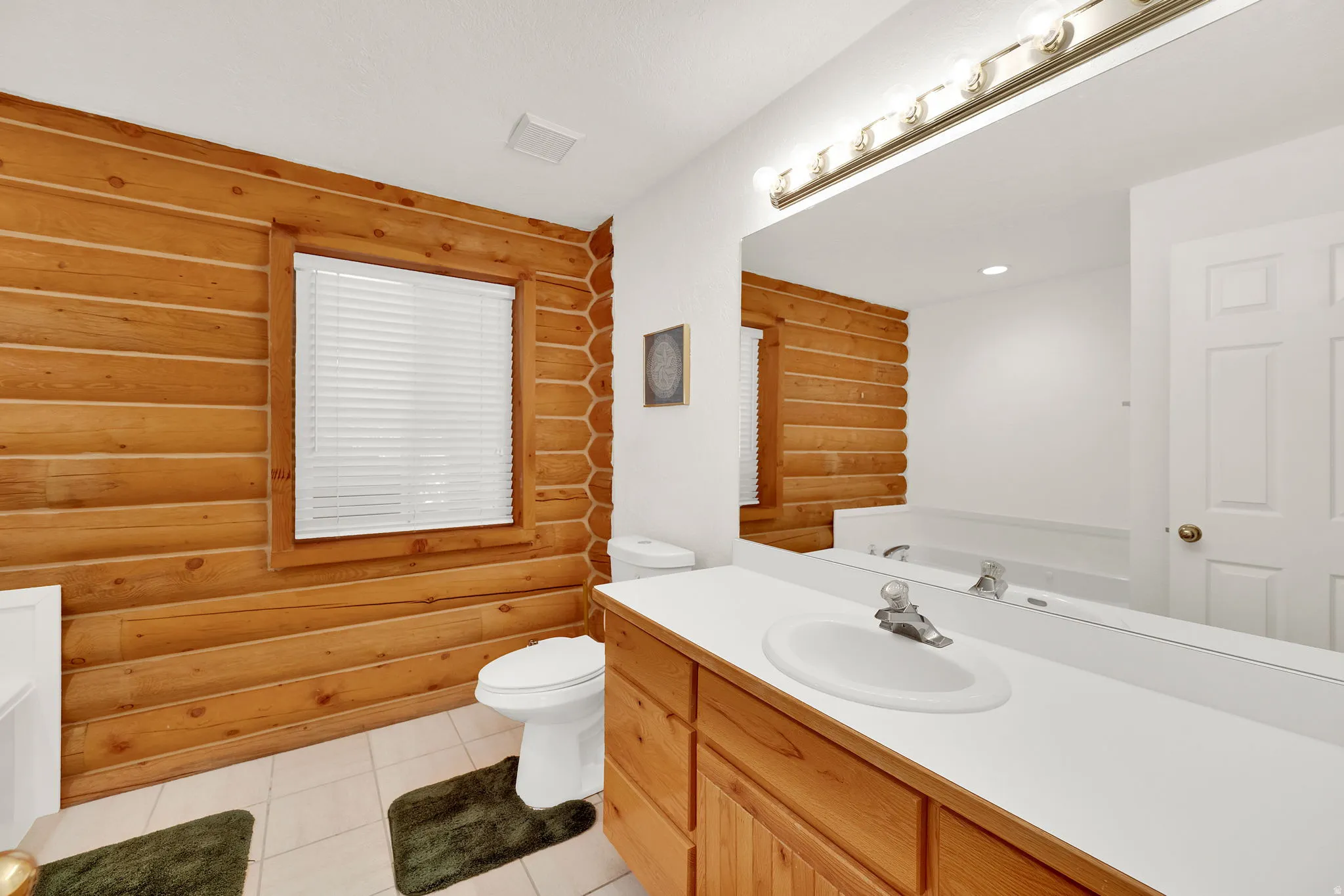 Bathroom featuring rustic walls, vanity, light tile patterned flooring, and a garden tub