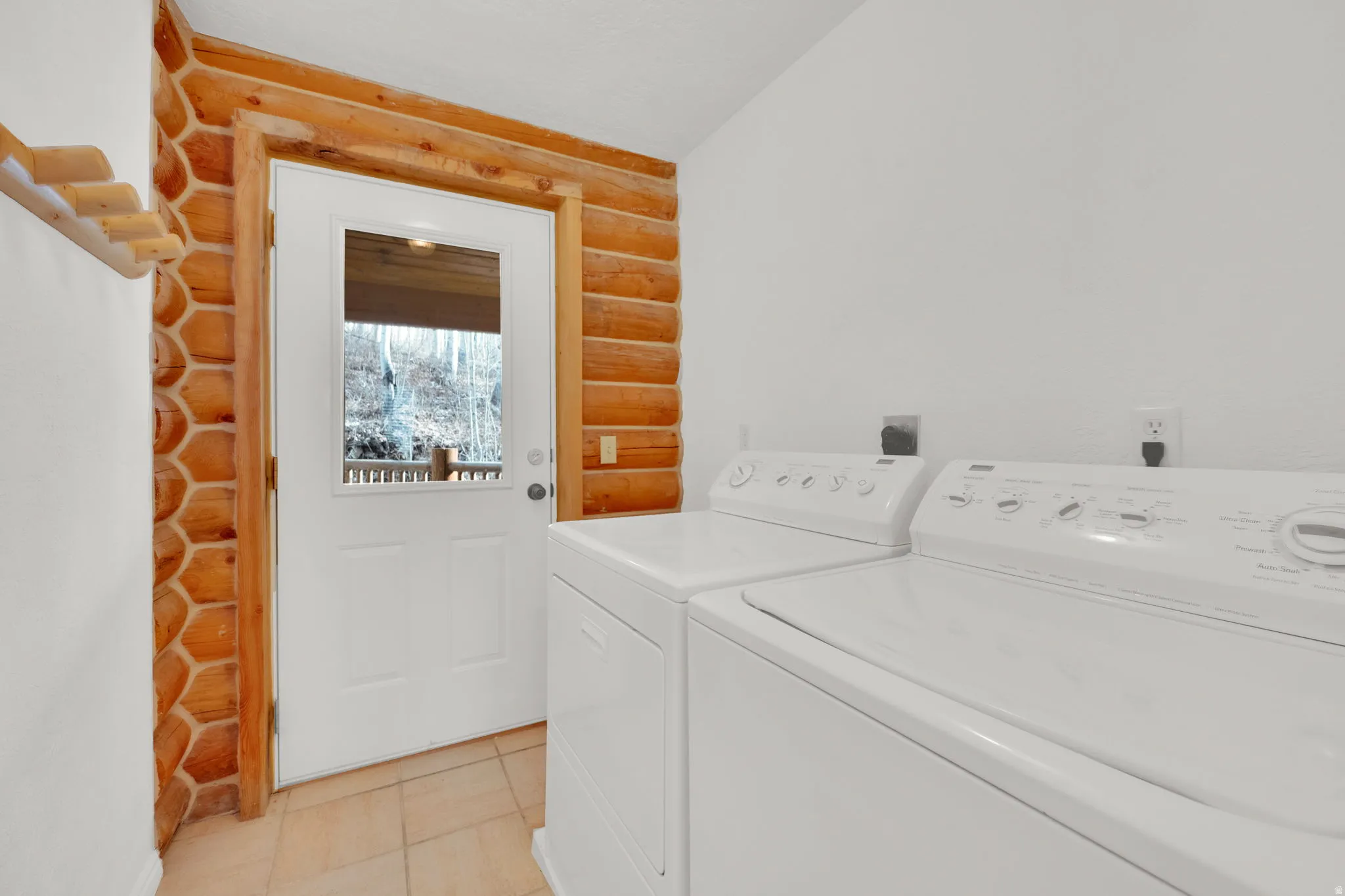 Laundry room with rustic walls, washer and dryer, and light tile patterned floors