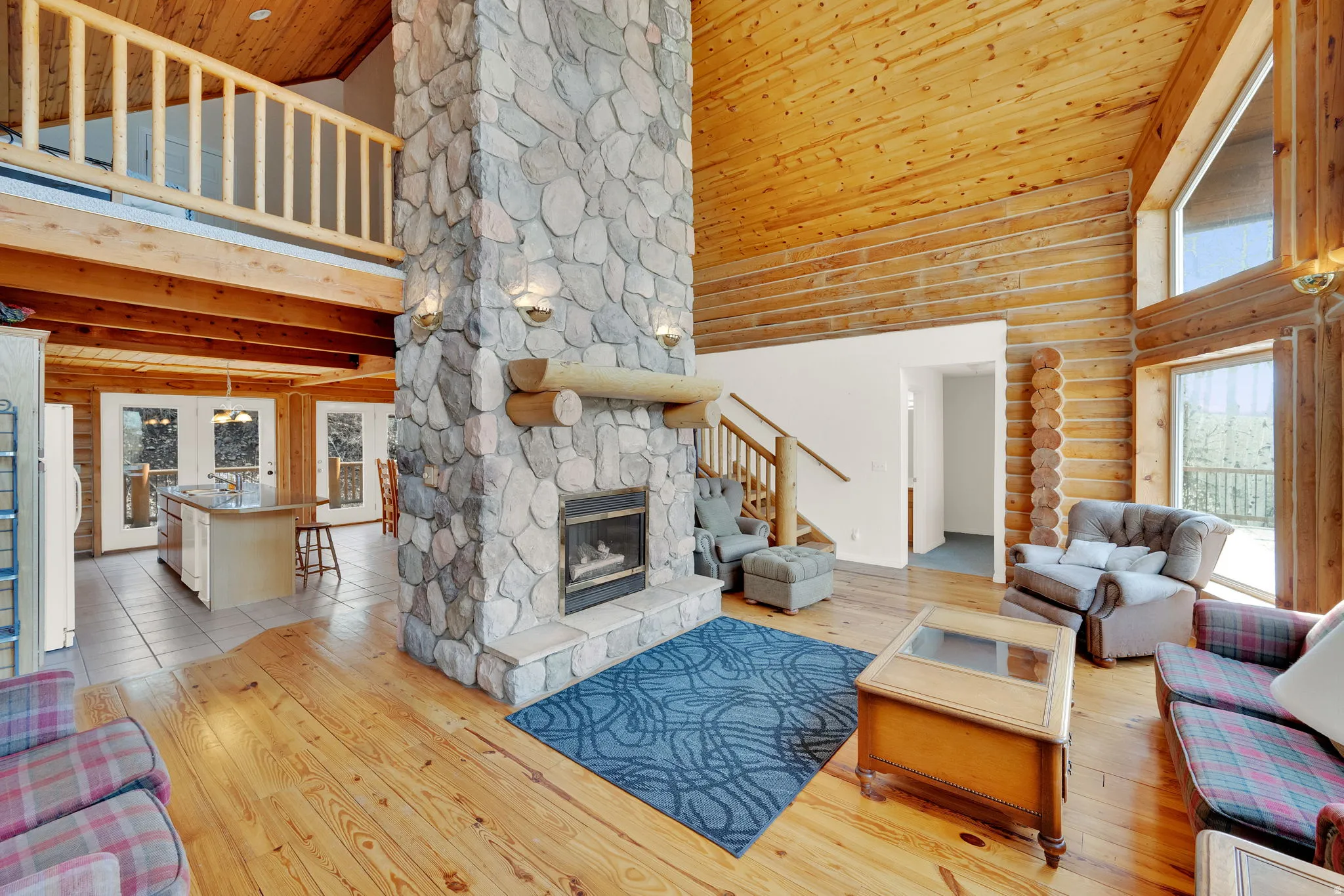 Living room with a high wood ceiling, light wood-style floors, a stone fireplace, and rustic walls