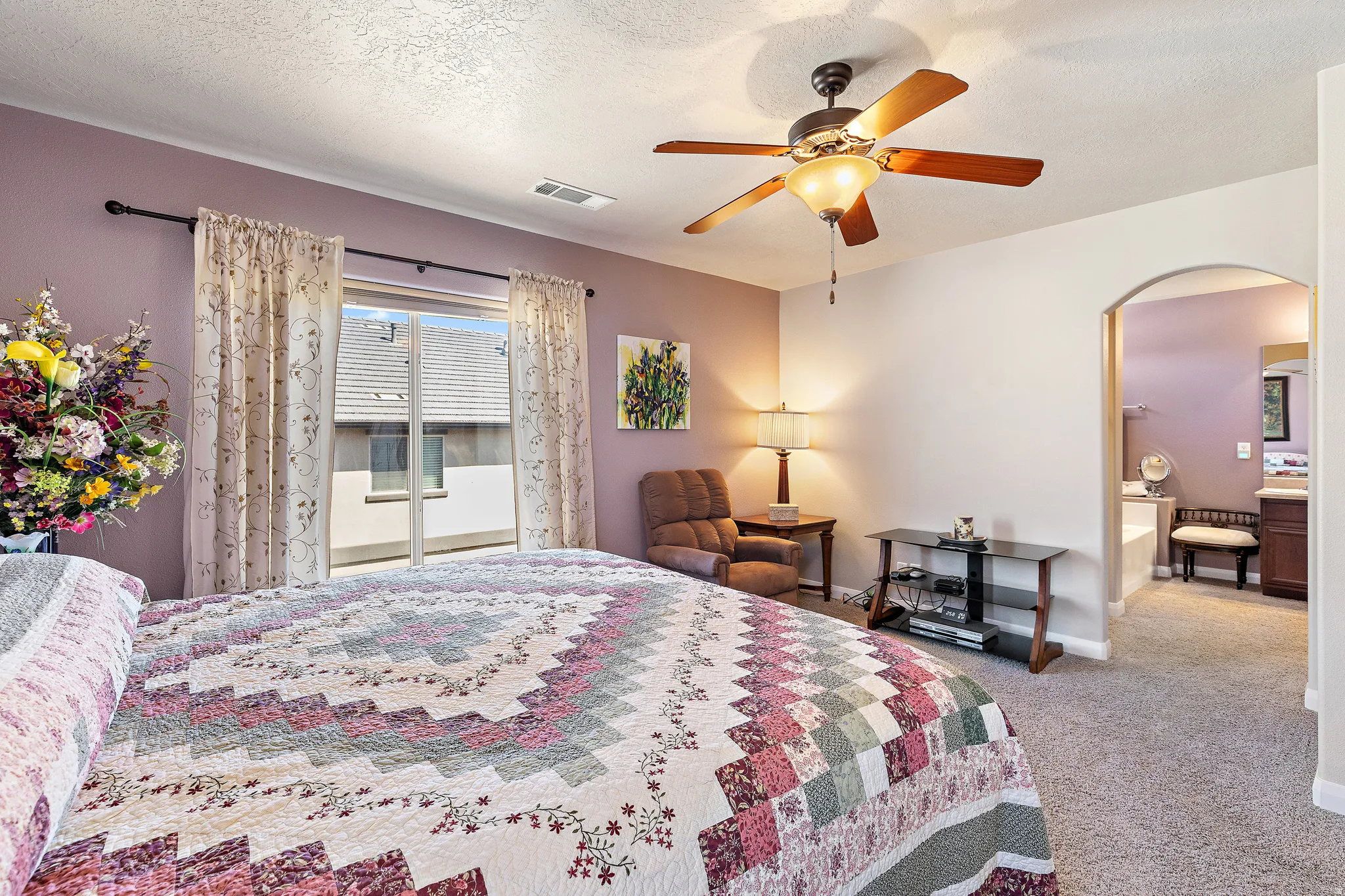 Carpeted bedroom featuring ensuite bath, arched walkways, ceiling fan, and a textured ceiling