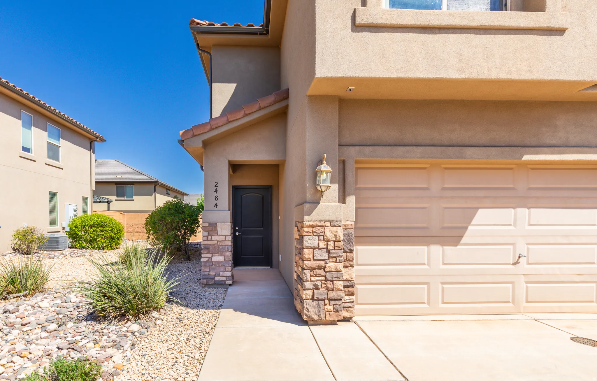 Property entrance with a garage, a tile roof, stucco siding, stone siding, and driveway