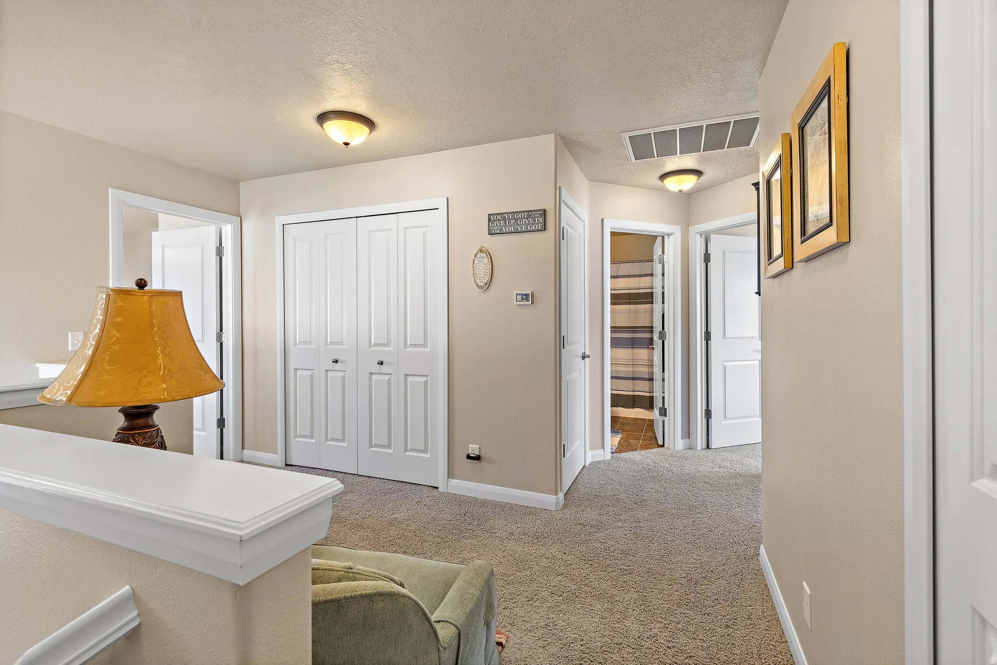 Hallway with light colored carpet and a textured ceiling