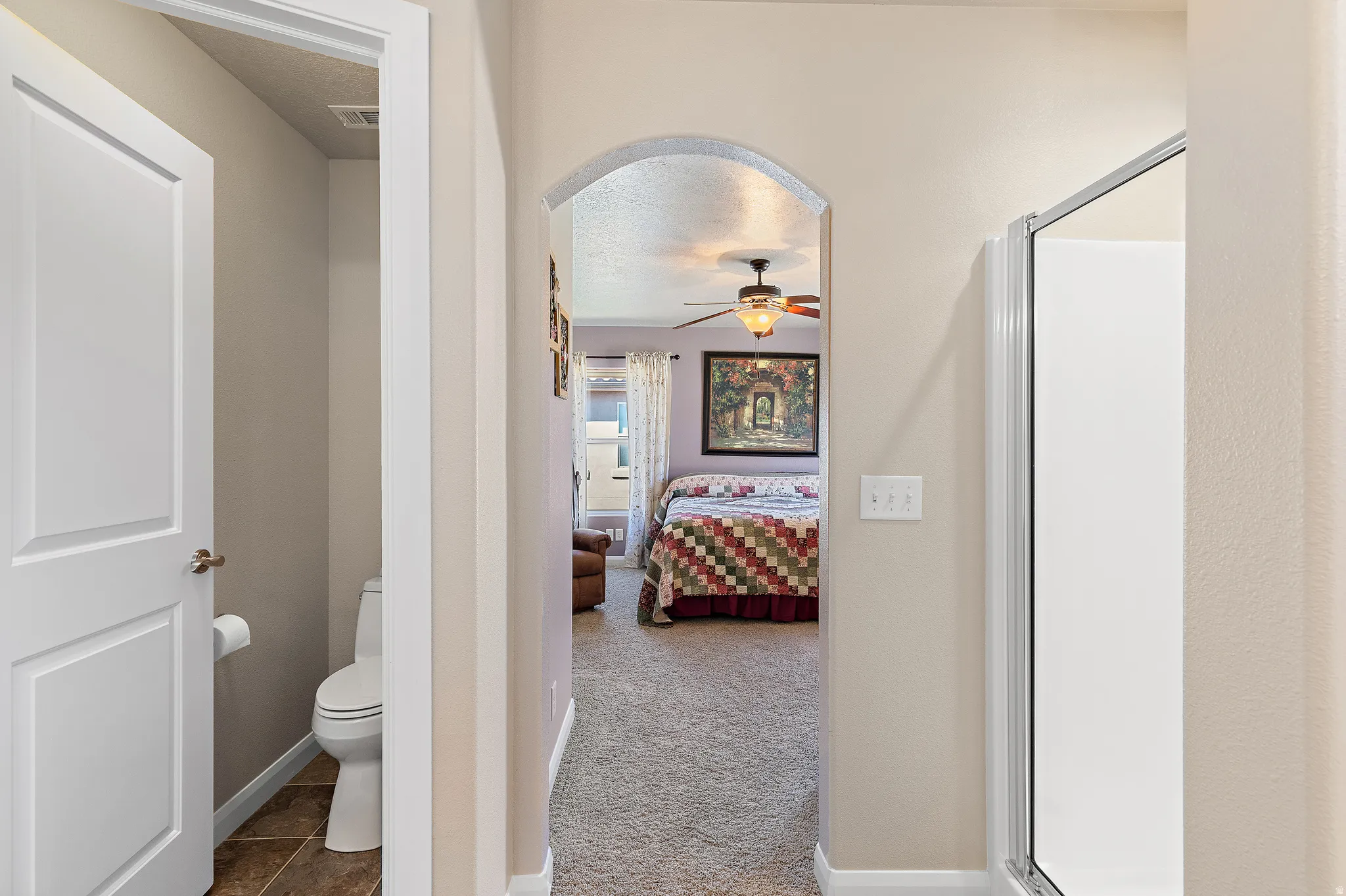 Ensuite bathroom featuring a shower stall, carpet, ceiling fan, a textured ceiling, and tile patterned flooring