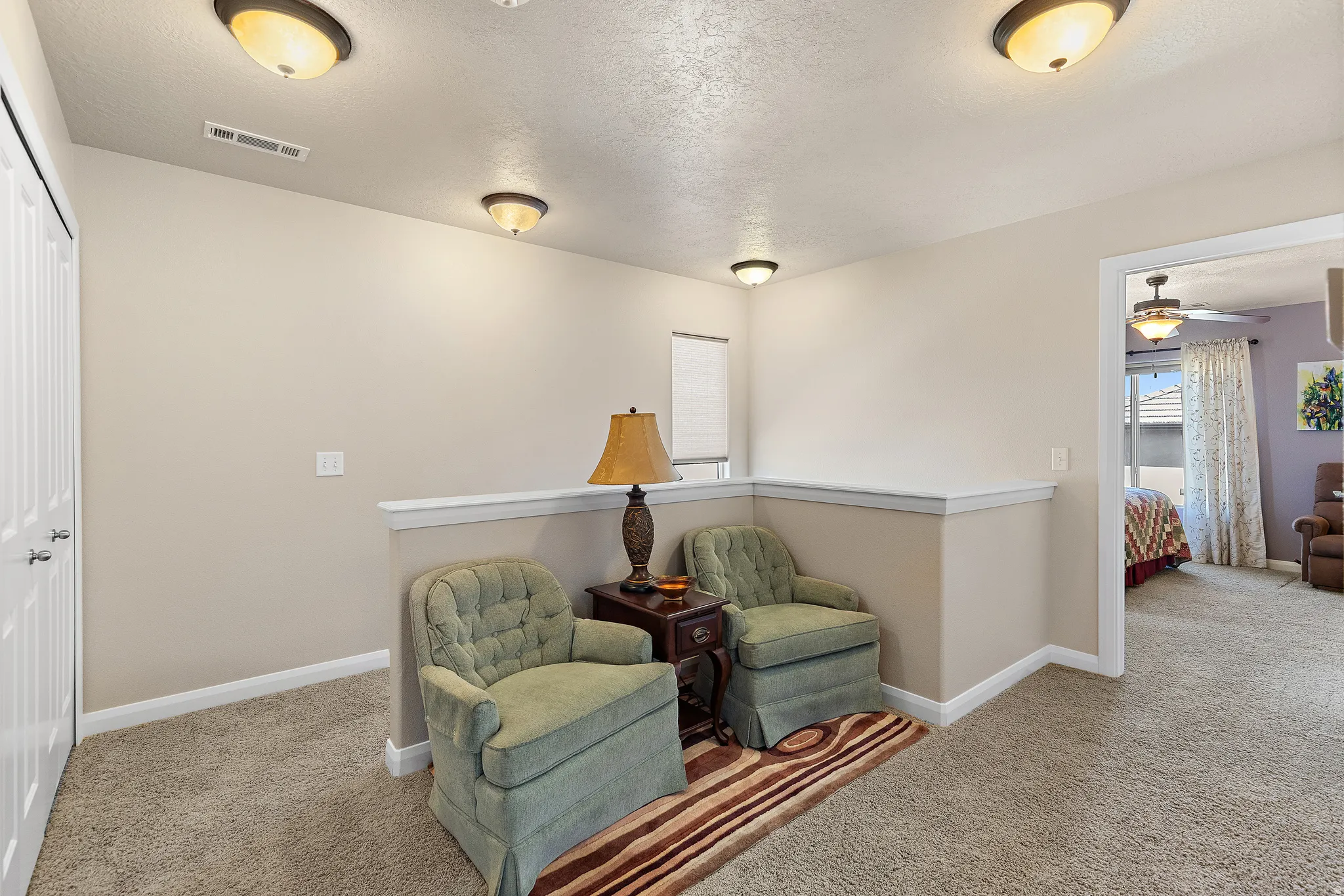 Living area featuring a textured ceiling, carpet, ceiling fan, and an upstairs landing