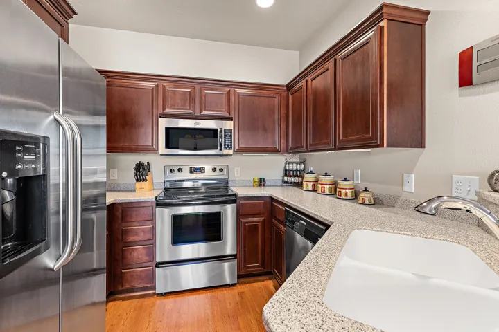 Kitchen with stainless steel appliances, light stone countertops, and light wood-style flooring