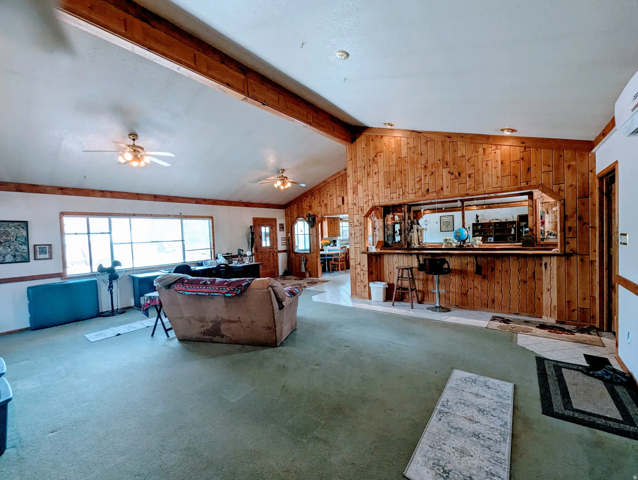 Carpeted living area with ceiling fan, beamed ceiling, and wooden walls