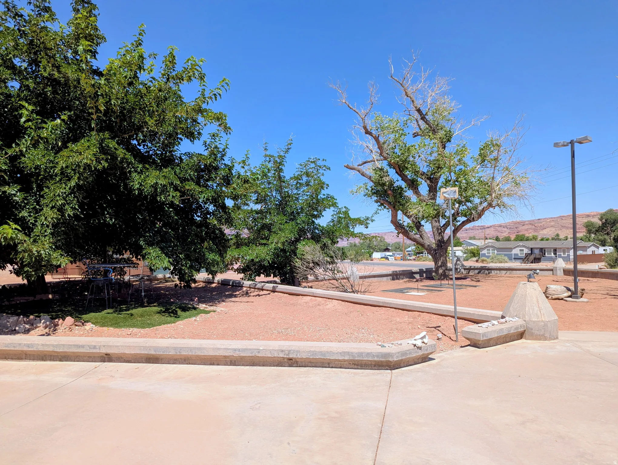 Spacious outdoor area with mature trees, a concrete walkway, and desert landscaping