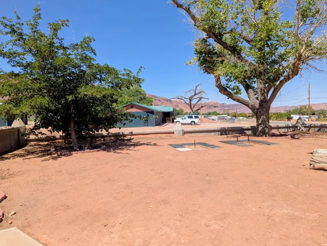 Spacious outdoor area with natural ground cover, mature shade trees, and built-in horseshoe pits