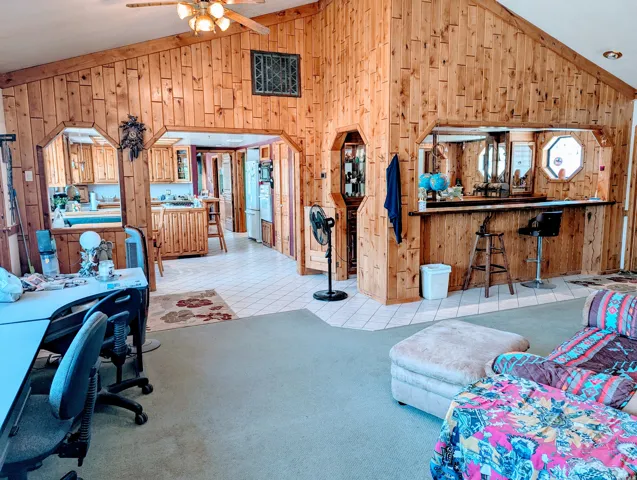 Living room with wooden walls, vaulted ceiling, arched walkways, a ceiling fan, and light tile patterned floors