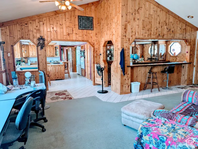 Living room with wooden walls, vaulted ceiling, arched walkways, a ceiling fan, and light tile patterned floors