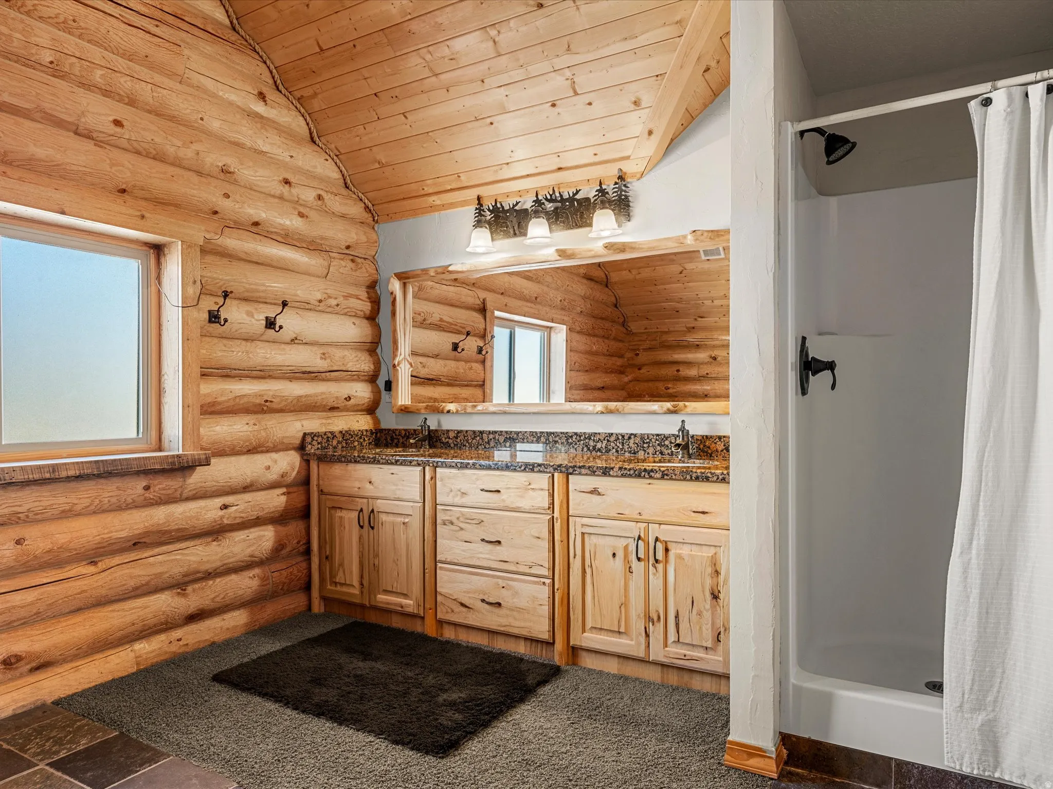 Full bath with a vaulted wood ceiling, double vanity, a shower stall, and log walls