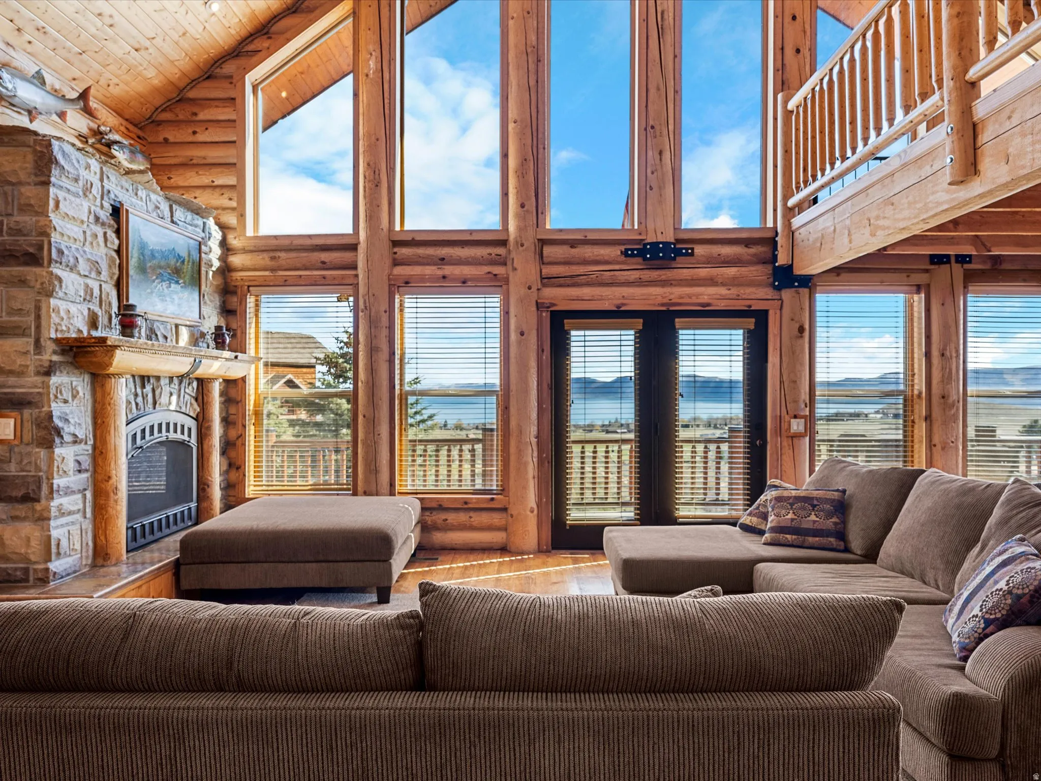 Living room featuring log walls, a stone fireplace, a vaulted wooden ceiling, and wood-type flooring