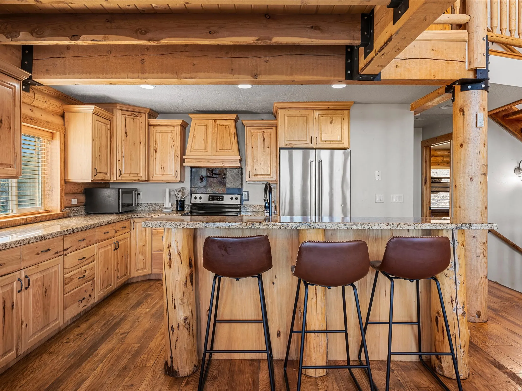 Kitchen with stainless steel appliances, light wood finish cabinetry, recessed lighting, light stone counters, and beam ceiling
