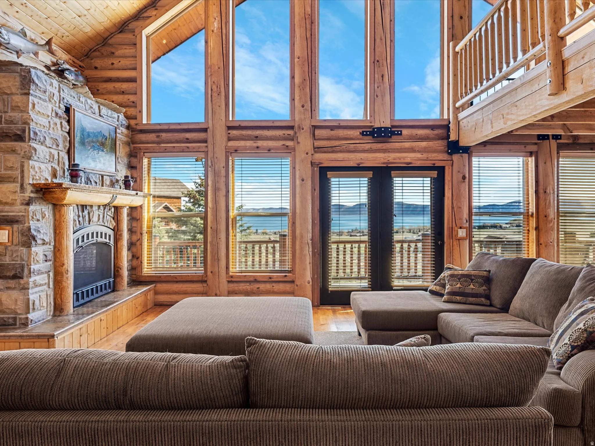 Living room with log walls, a fireplace, a vaulted wooden ceiling, wood finished floors, and a water view