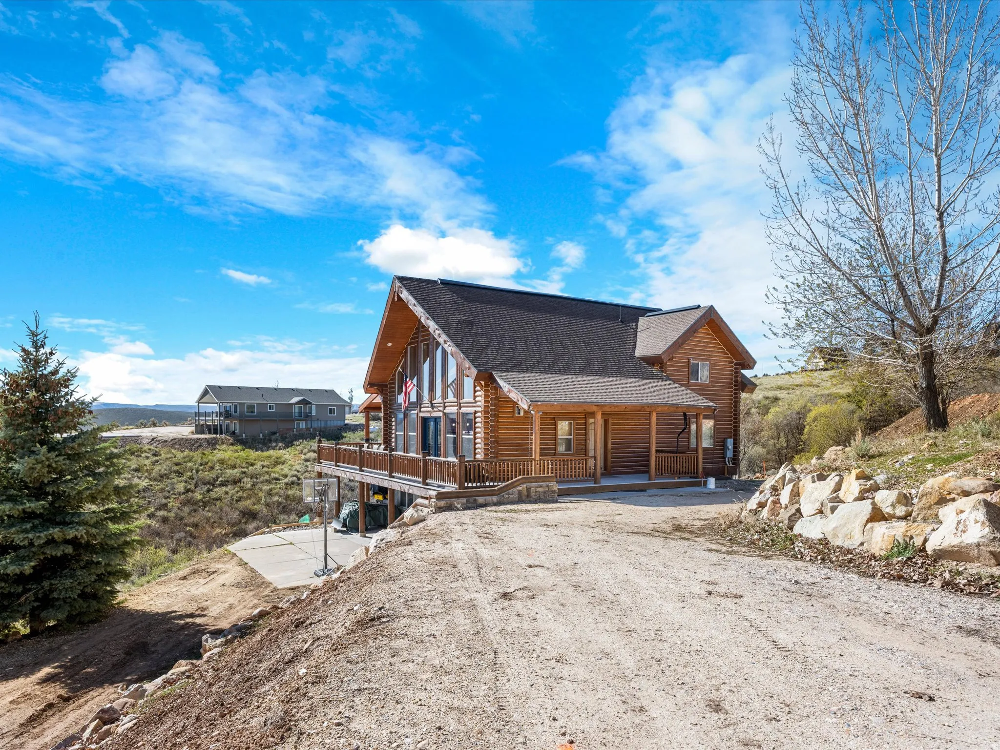 View of front of house featuring log exterior, a shingled roof, driveway, and a wooden deck