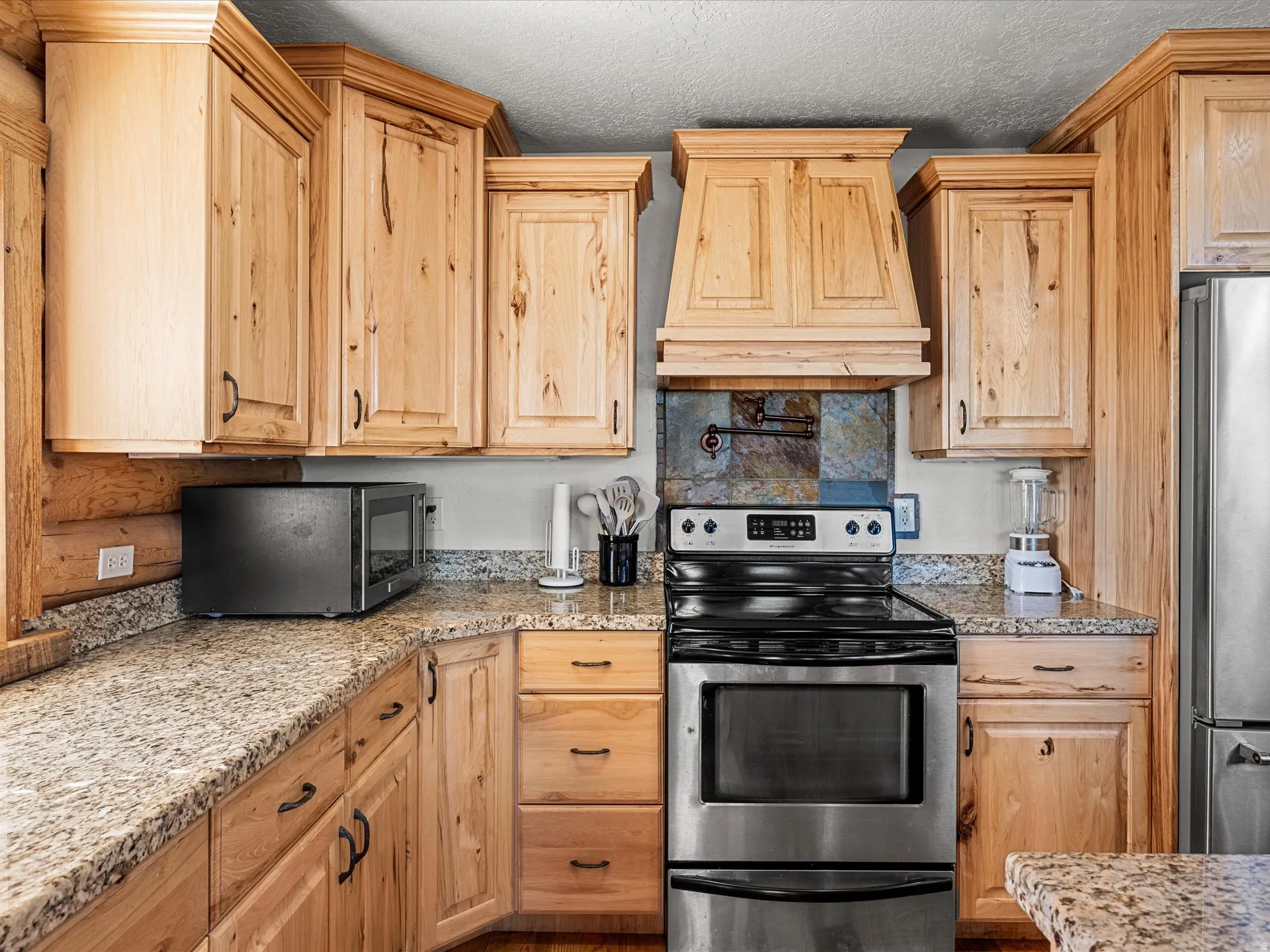Kitchen with stainless steel appliances, light stone countertops, light wood finish cabinets, and a textured ceiling
