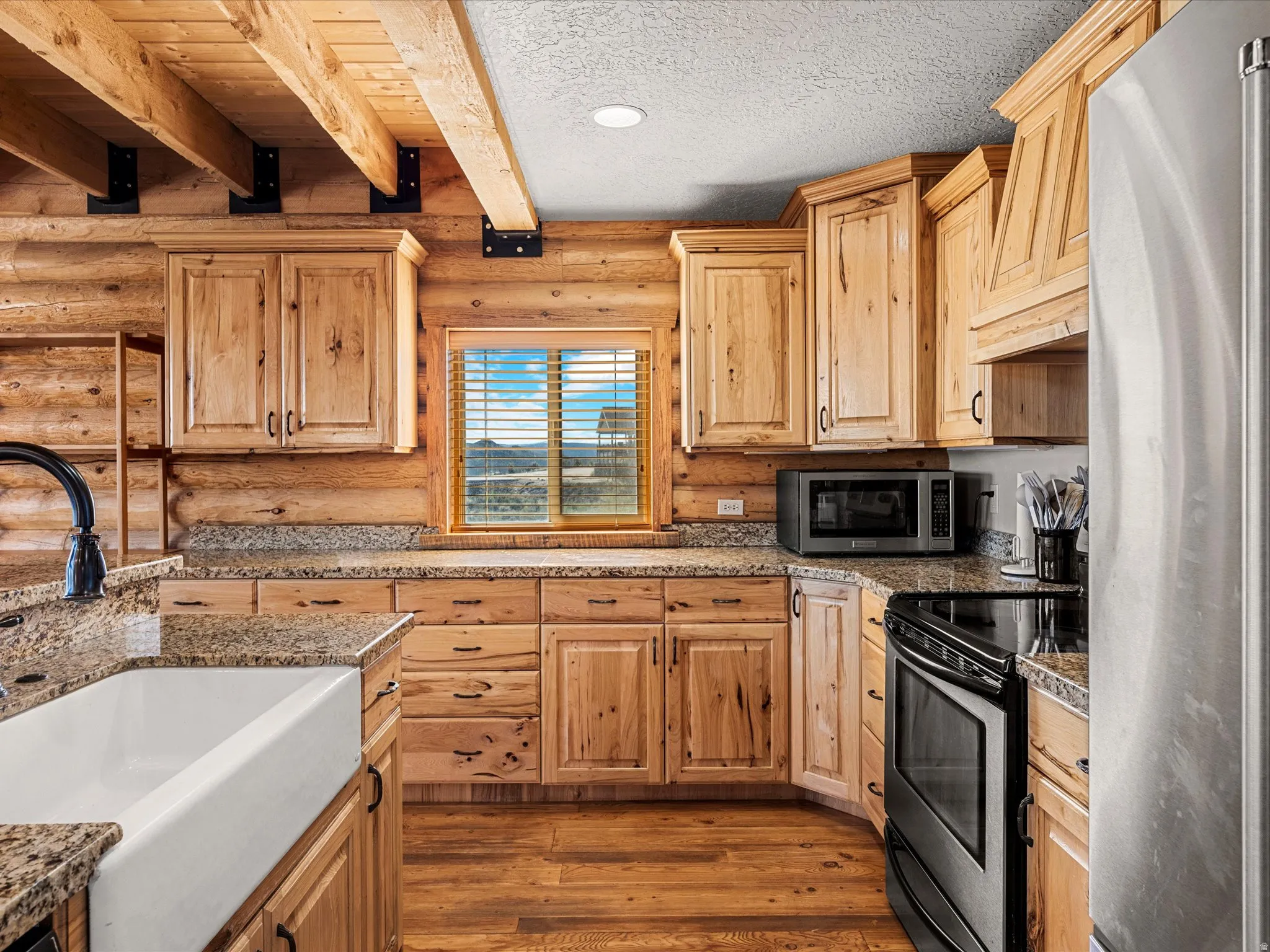 Kitchen featuring rustic walls, stainless steel appliances, dark wood finished floors, light wood finish cabinets, and beam ceiling