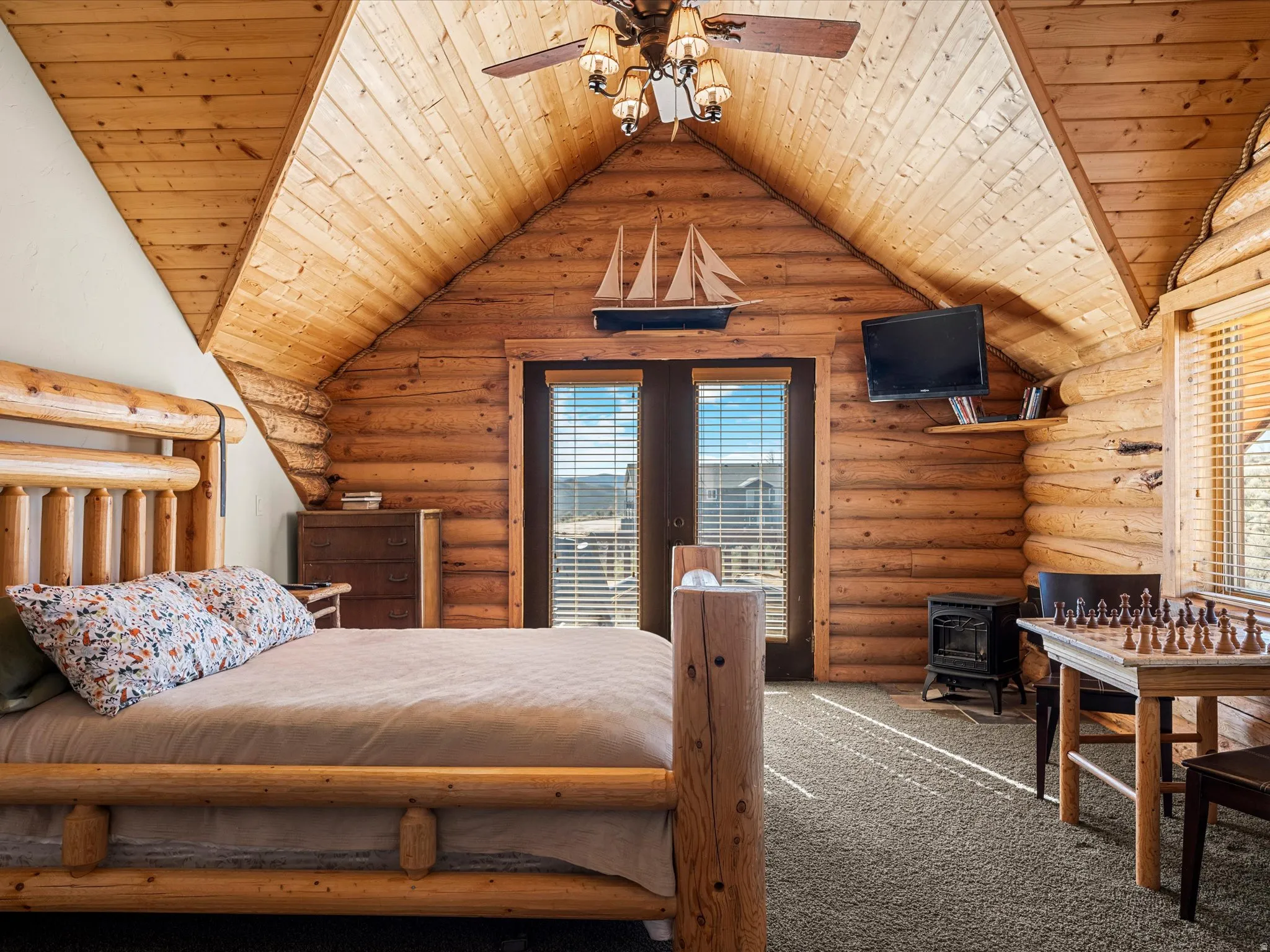 Bedroom with wooden ceiling, rustic walls, multiple windows, french doors, and carpet floors