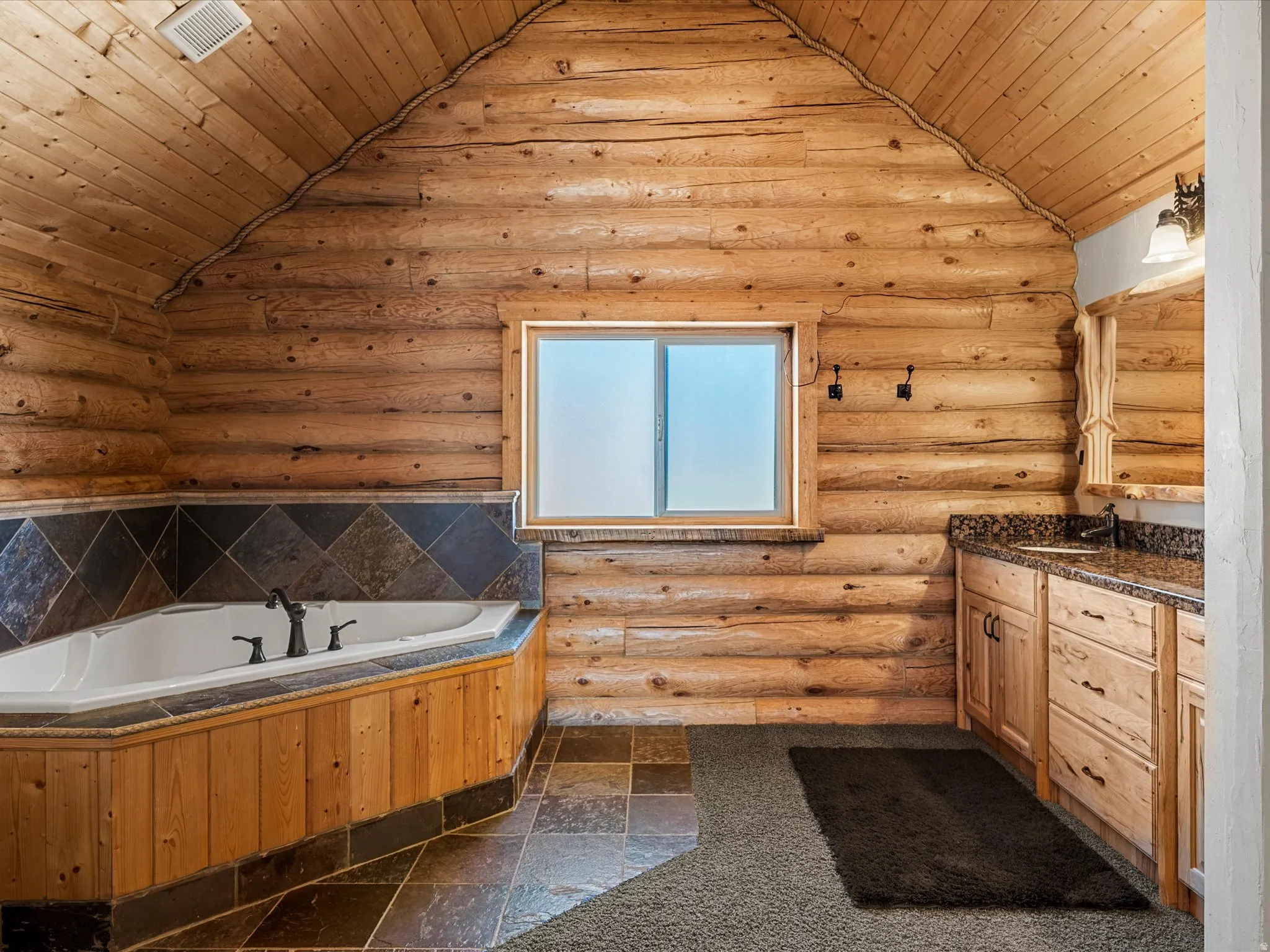 Bathroom featuring vanity, stone tile flooring, a vaulted wood ceiling, log walls, and a bath
