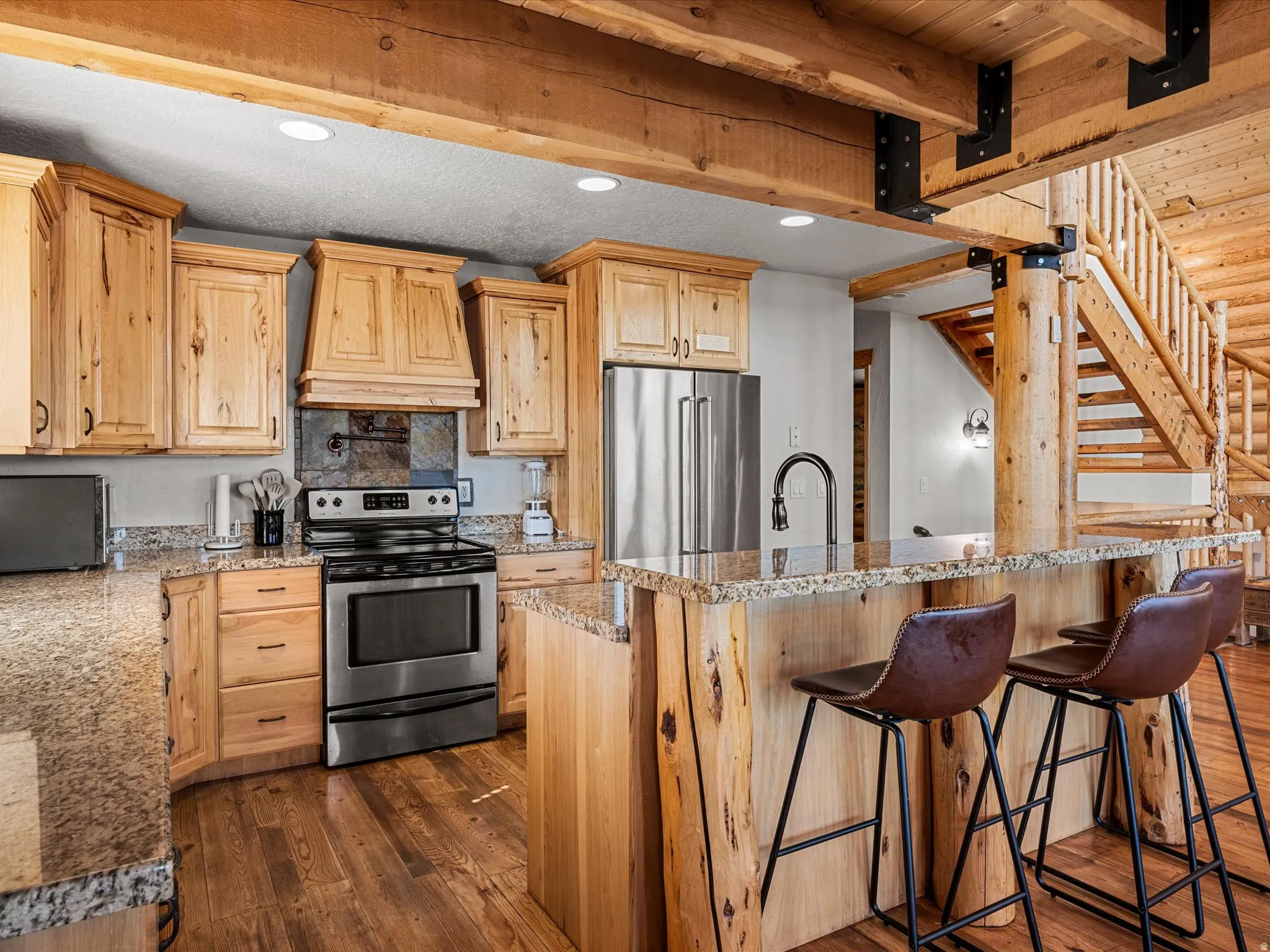 Kitchen featuring light wood finish cabinetry, stainless steel appliances, dark wood-type flooring, a center island with sink, and light stone countertops