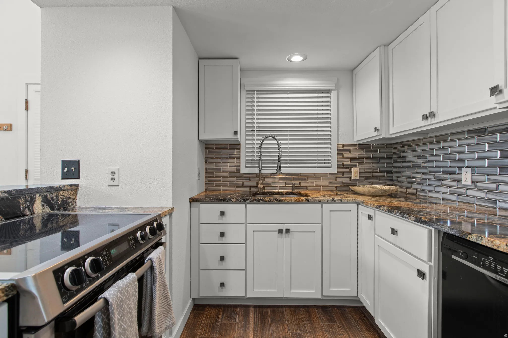 Kitchen featuring stainless steel electric range, dark stone counters, white cabinetry, black dishwasher, and dark wood-style floors