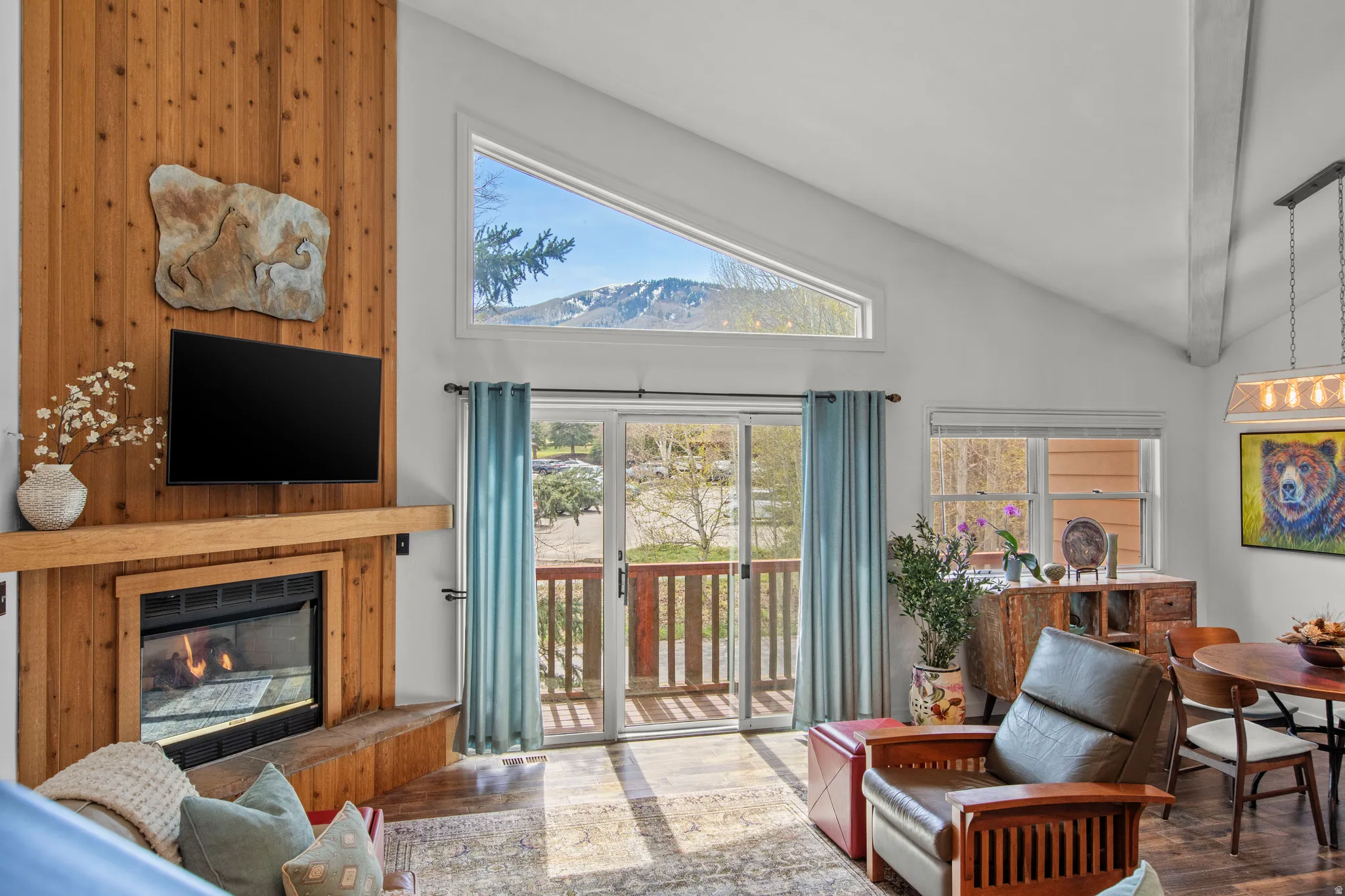 Living room with a glass covered fireplace, wood finished floors, healthy amount of natural light, and lofted ceiling
