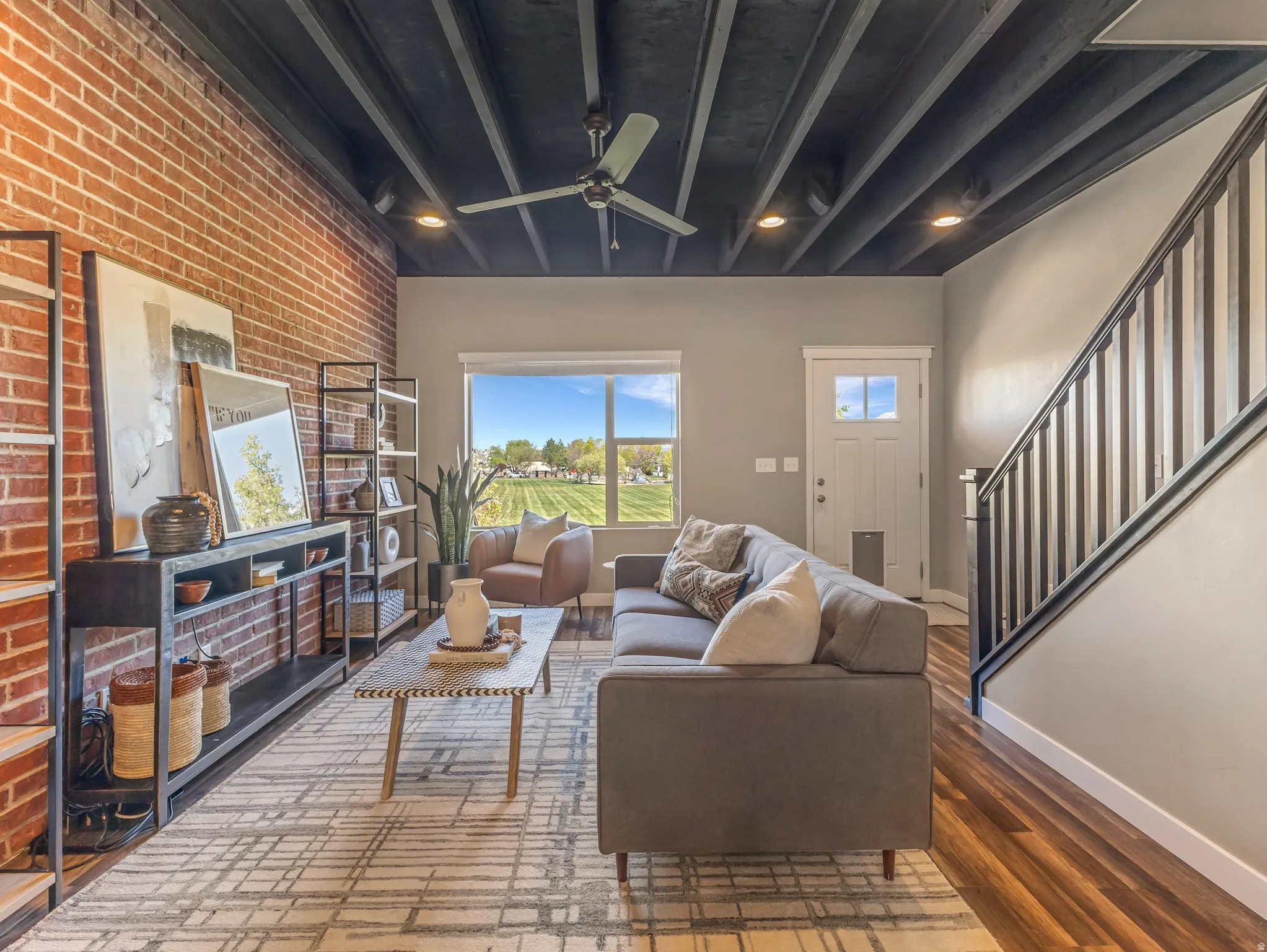 Living area featuring a ceiling fan, wood finished floors, brick wall, and beam ceiling