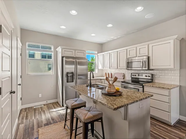 Kitchen with stainless steel appliances, a kitchen breakfast bar, light stone counters, tasteful backsplash, and white cabinets
