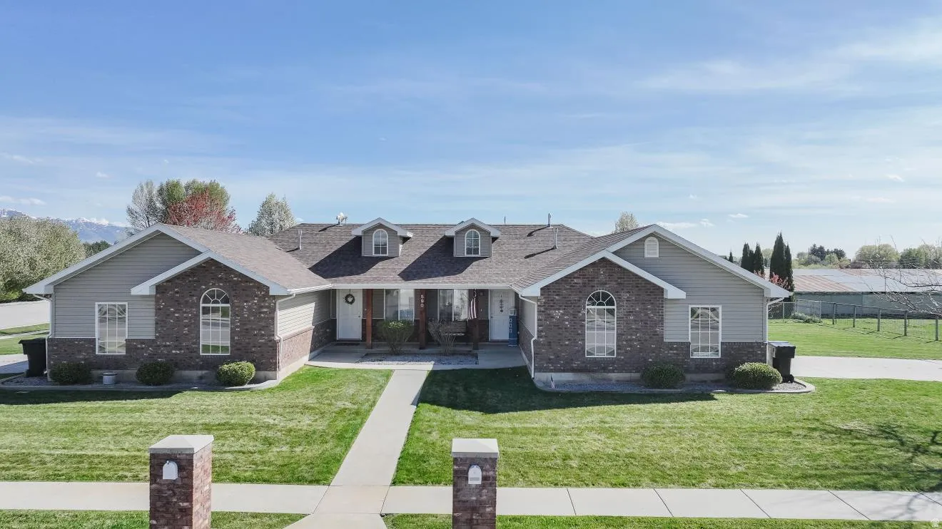 View of front facade featuring a porch, brick siding, a front lawn, and roof with shingles