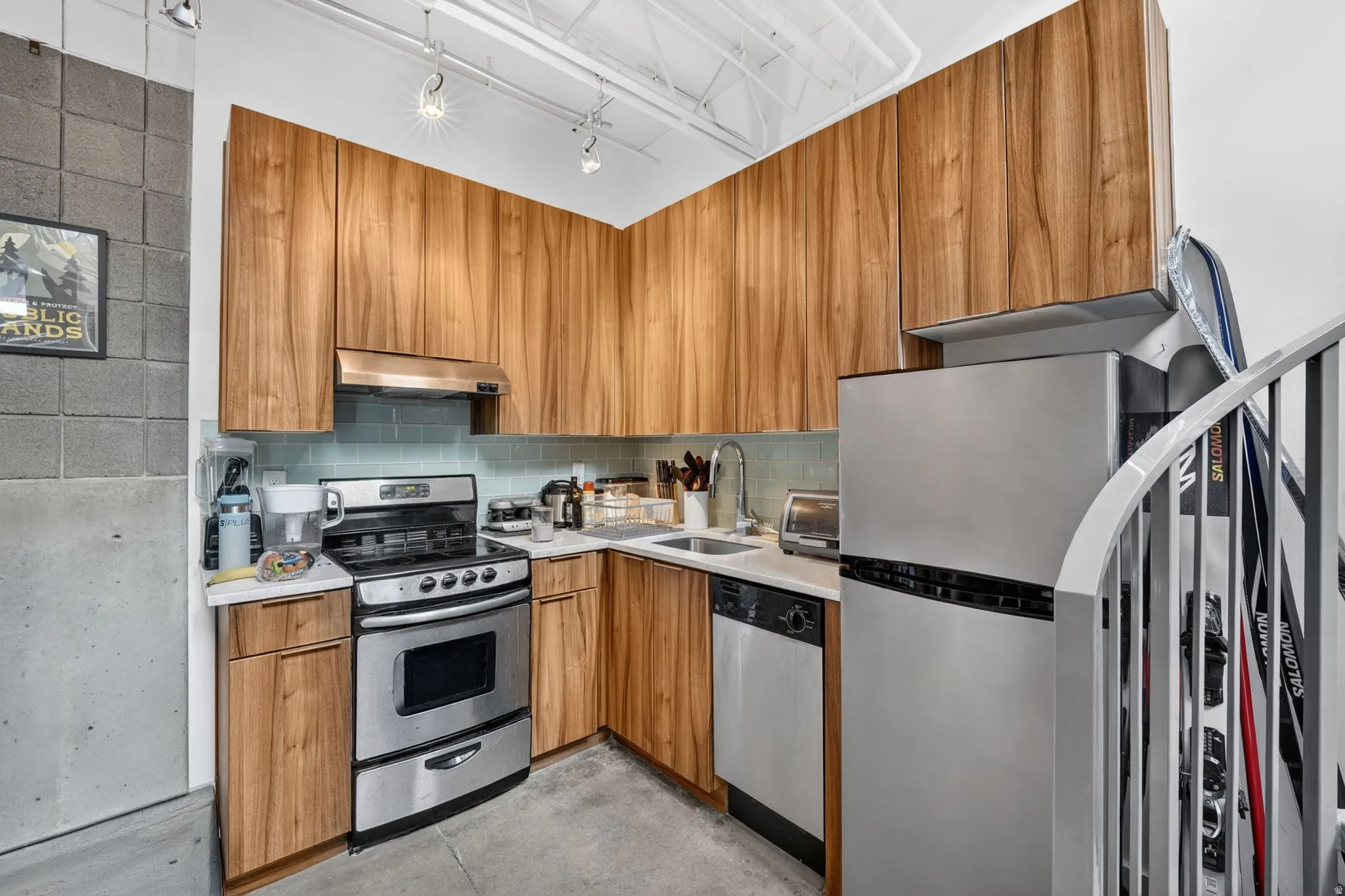 Kitchen with stainless steel appliances, light countertops, tasteful backsplash, wood finish cabinetry, and track lighting