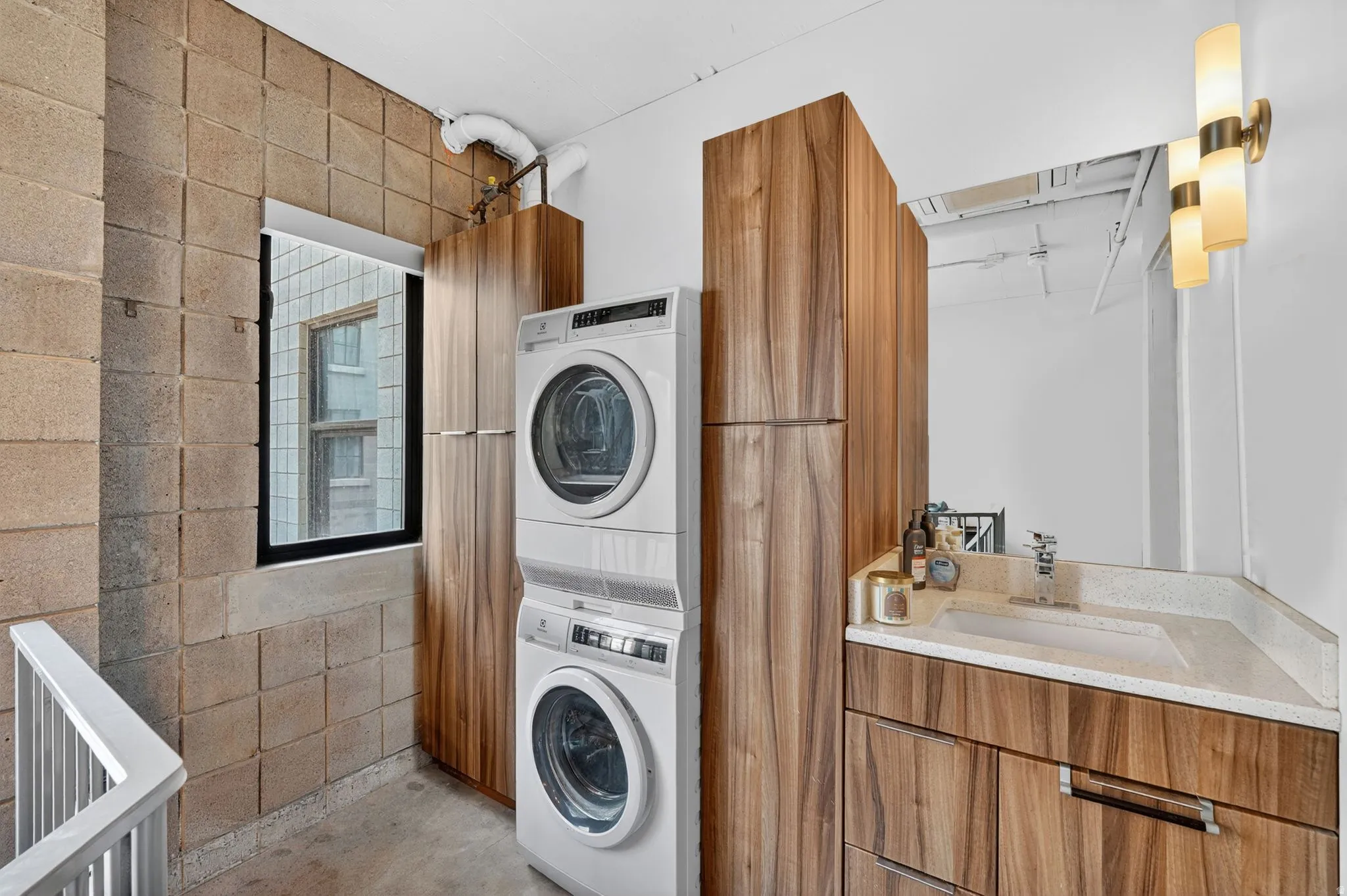 Laundry area featuring concrete flooring, stacked washing machine and dryer, and concrete block wall