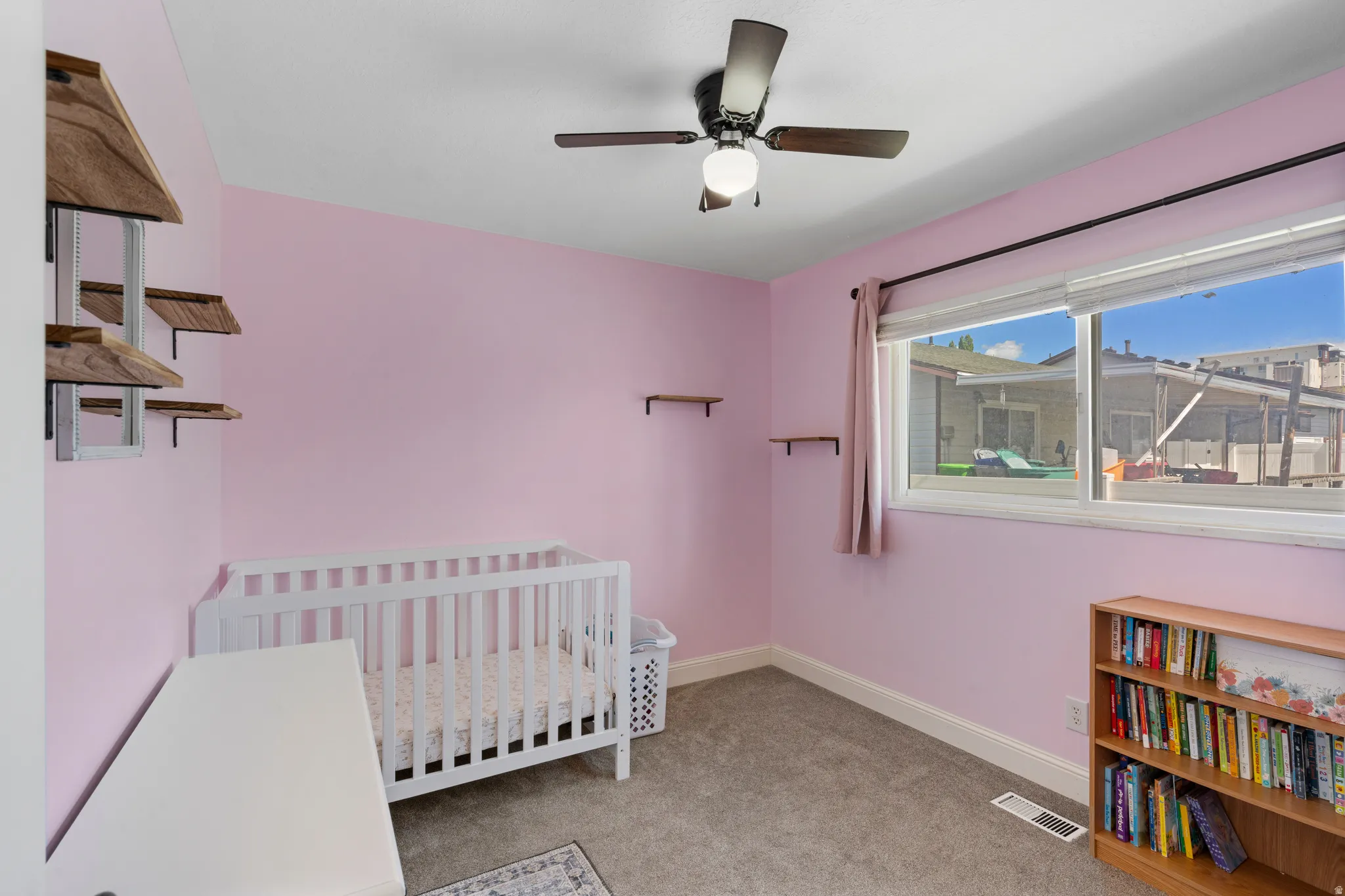Bedroom featuring light colored carpet, a nursery area, and a ceiling fan