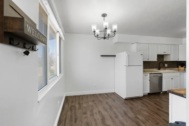 Kitchen with freestanding refrigerator, white cabinets, dishwasher, dark wood-style floors, and hanging lights