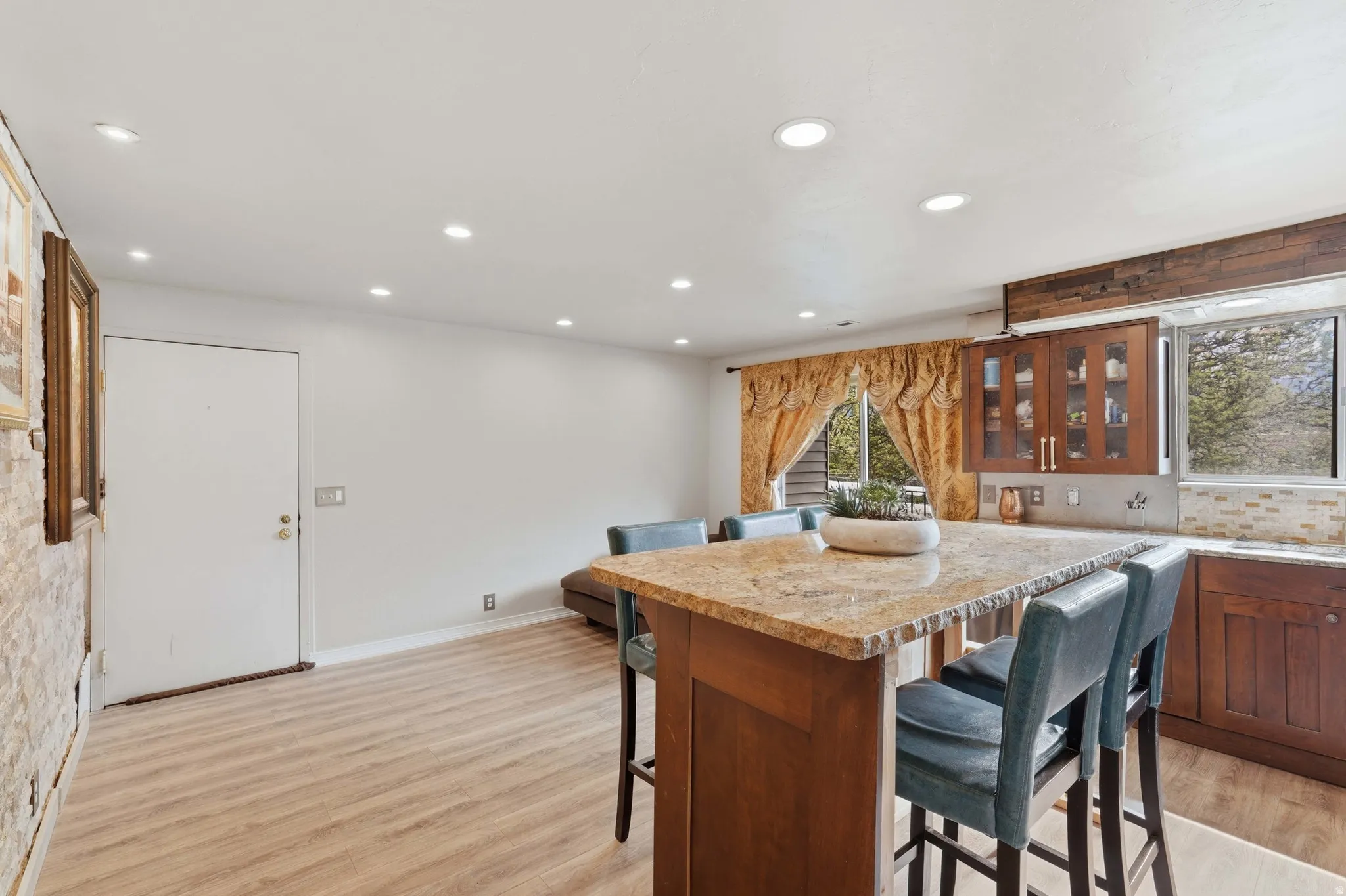 Kitchen with glass fronted cabinets, a breakfast bar, light wood-style floors, wood finish cabinets, and light stone counters