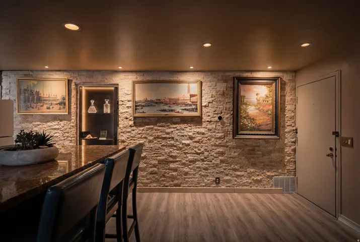 Indoor wet bar with dark wood-type flooring, dark stone counters, and recessed lighting