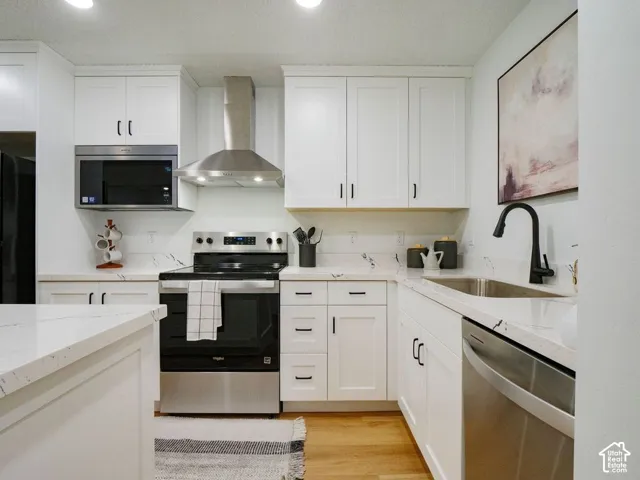 Kitchen with stainless steel appliances, white cabinets, light stone countertops, light wood-style flooring, and recessed lighting
