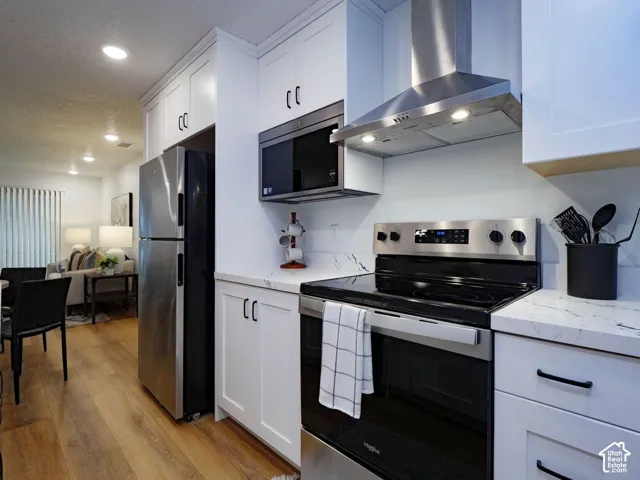 Kitchen featuring stainless steel appliances, white cabinetry, light stone counters, light wood-style flooring, and recessed lighting