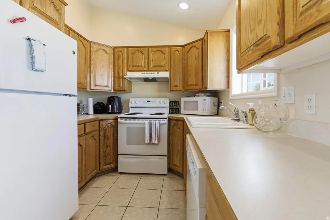 Kitchen with white appliances, light countertops, wood finish cabinetry, light tile patterned floors, and vaulted ceiling