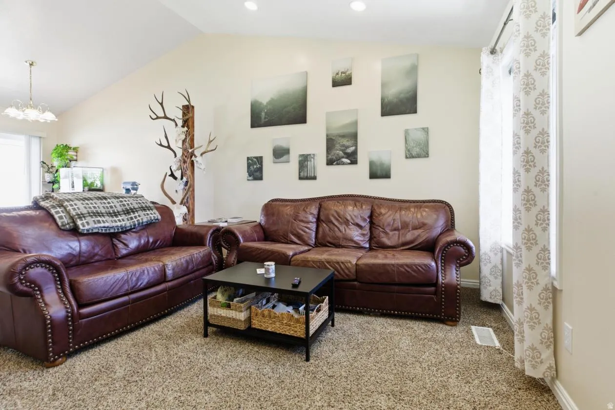 Living area featuring light carpet, healthy amount of natural light, lofted ceiling, and a chandelier