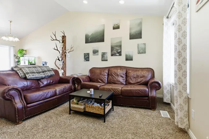 Living area featuring light carpet, healthy amount of natural light, lofted ceiling, and a chandelier