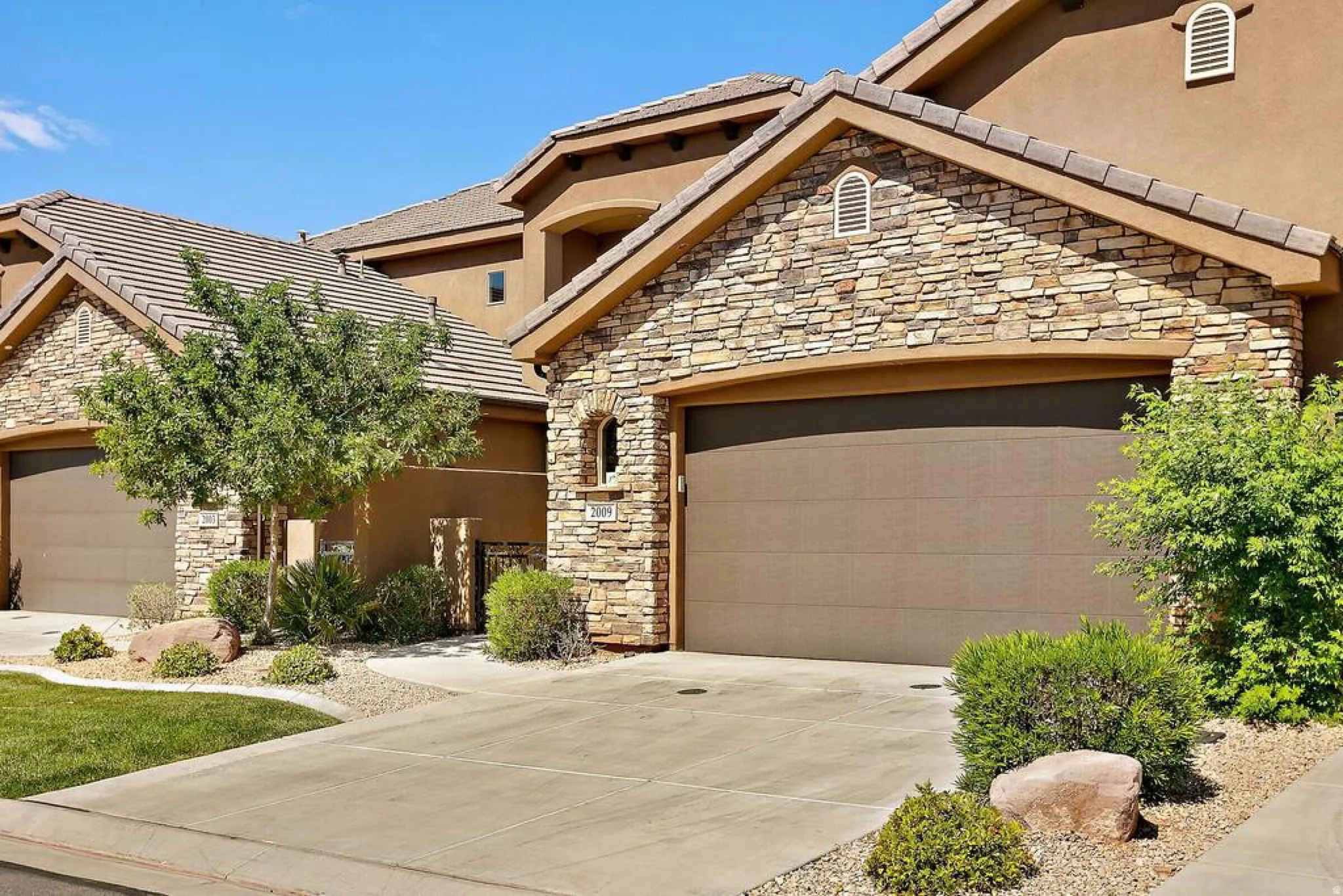 Mediterranean / spanish house with stone siding, a garage, stucco siding, and concrete driveway