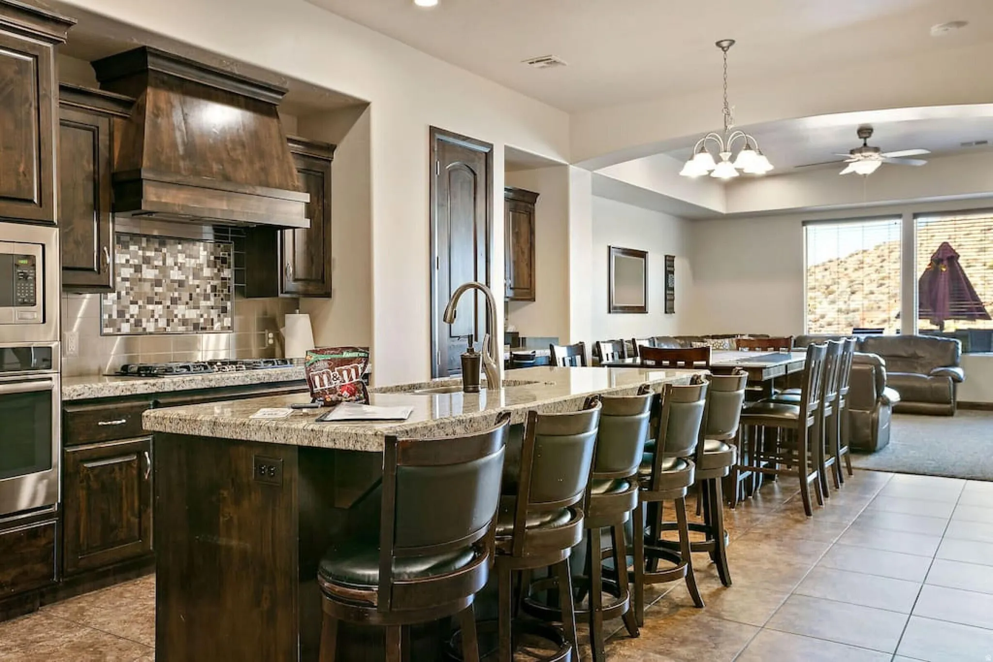 Kitchen featuring dark wood finish cabinetry, a ceiling fan, light stone countertops, open floor plan, and stainless steel appliances