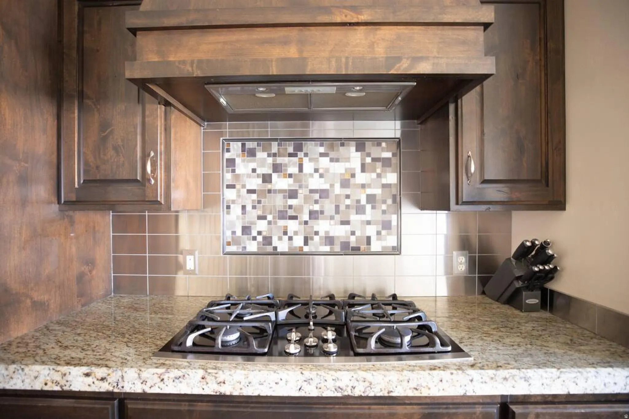 Kitchen with dark wood finish cabinetry, stainless steel gas cooktop, tasteful backsplash, and light stone countertops