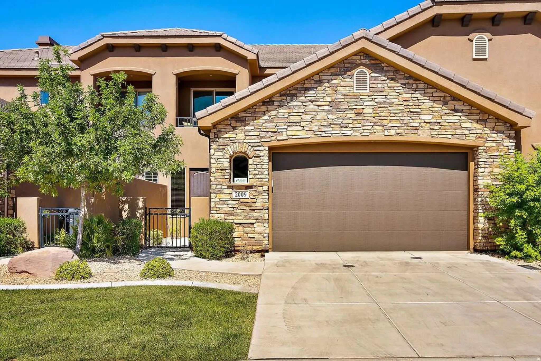 Mediterranean / spanish-style house with a garage, stone siding, driveway, stucco siding, and a gate