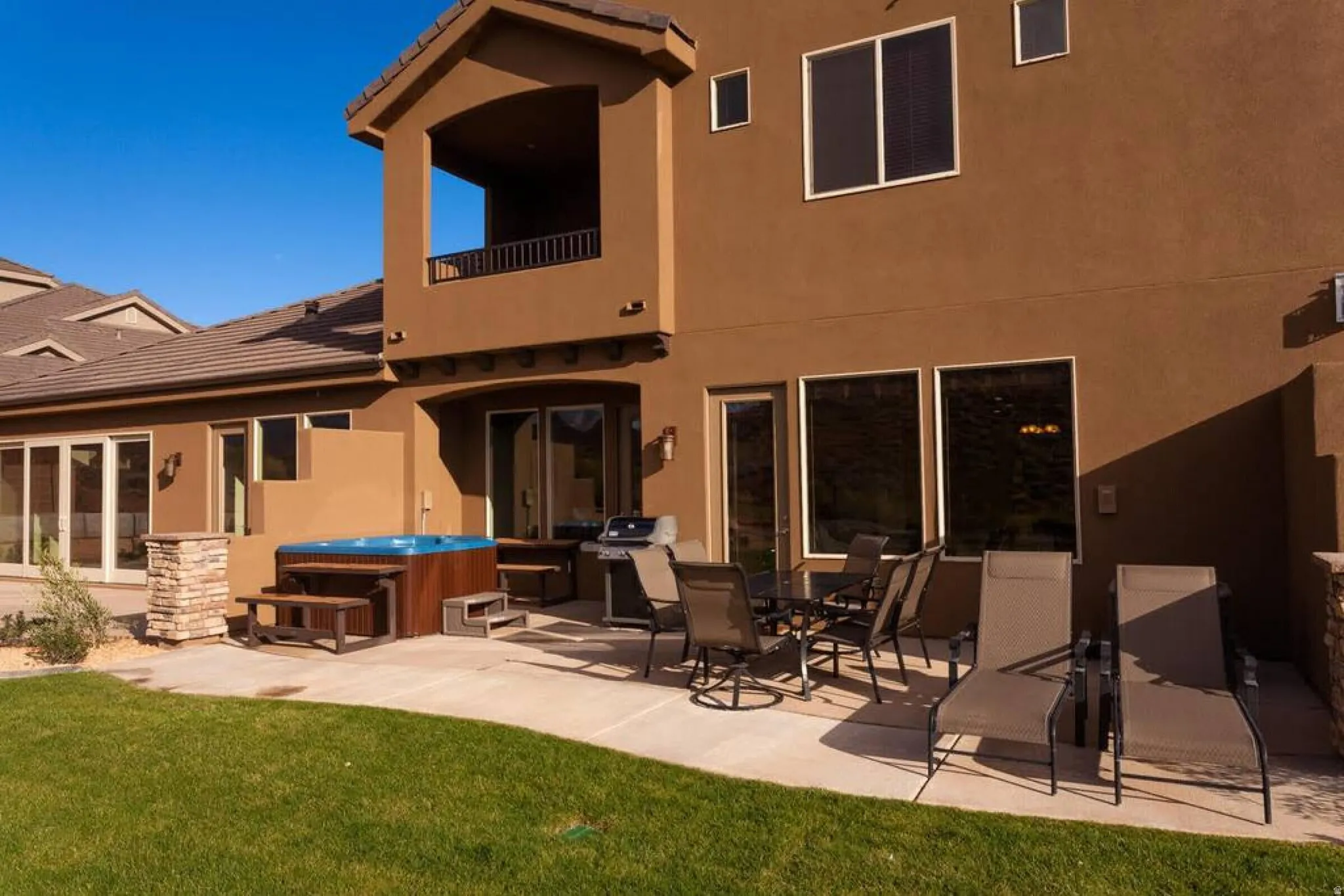 Rear view of property featuring a balcony, a hot tub, stucco siding, a patio area, and outdoor dining space
