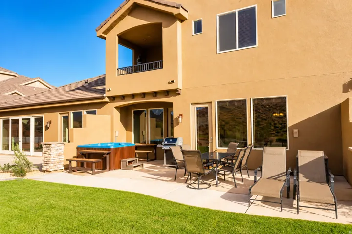 Manicured lawn with a concrete patio, built-in hot tub, and upper-level balcony